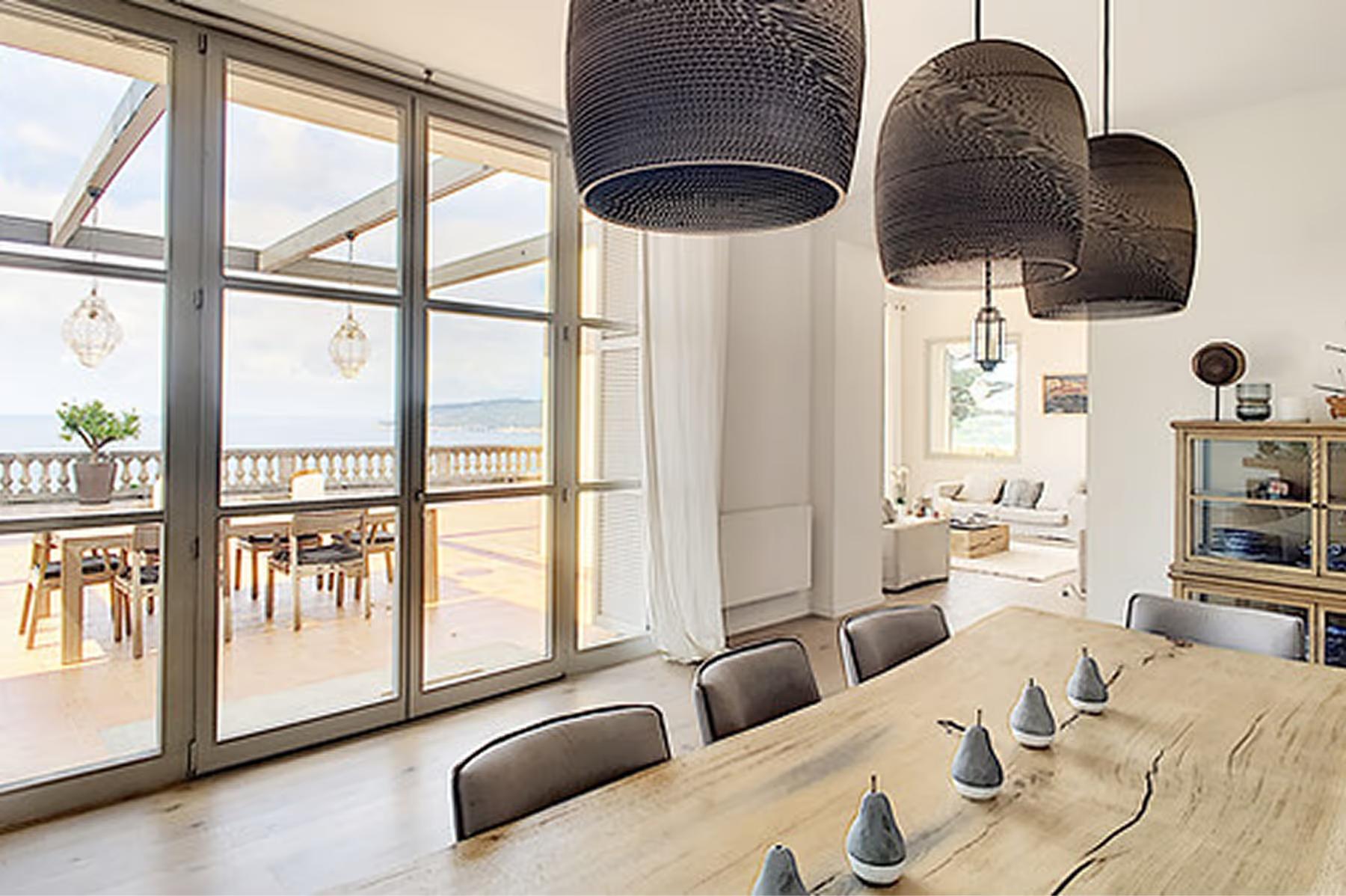 Le Domaine de Canaille: dining room with beige walls, wooden table, and pendant light fixtures, coastal views beyond