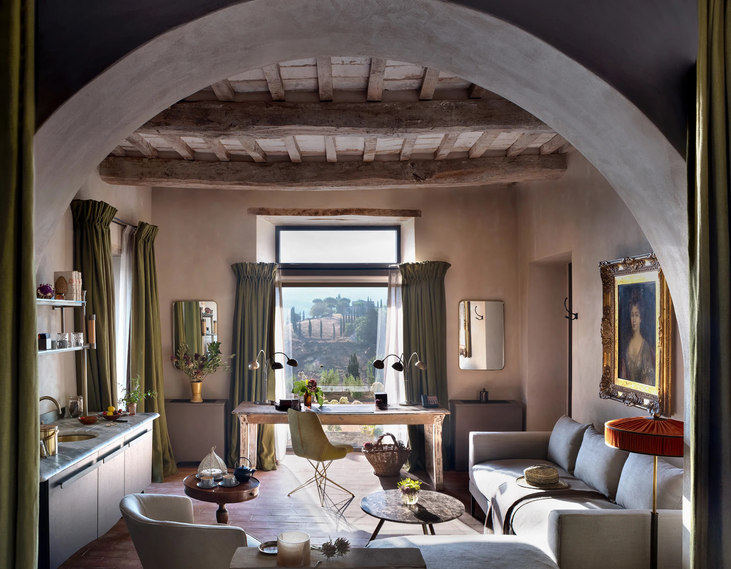 Castello di Reschio: a suite living area framed by a stone archway, with a sofa, dining table, and timber beam ceiling