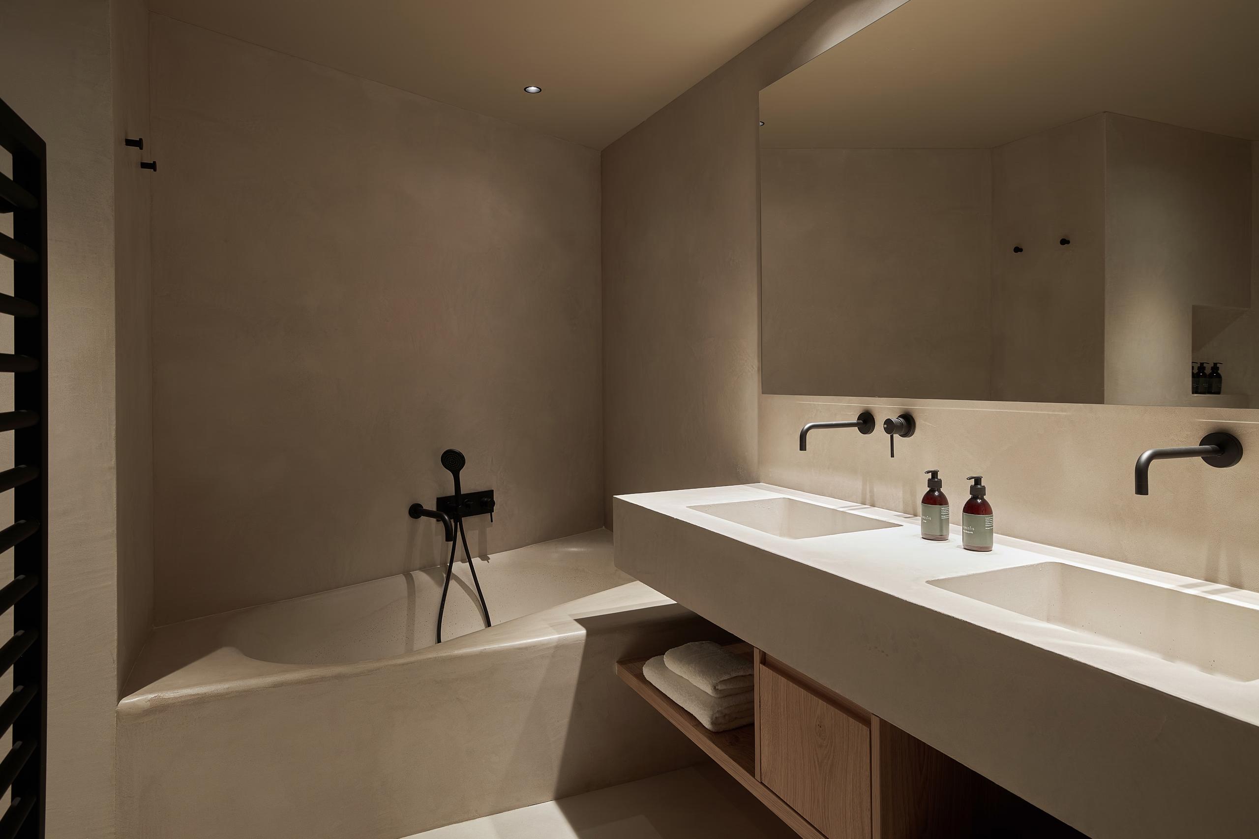A minimalist bathroom with concrete and natural wood vanity, white fixtures, and soft lighting
