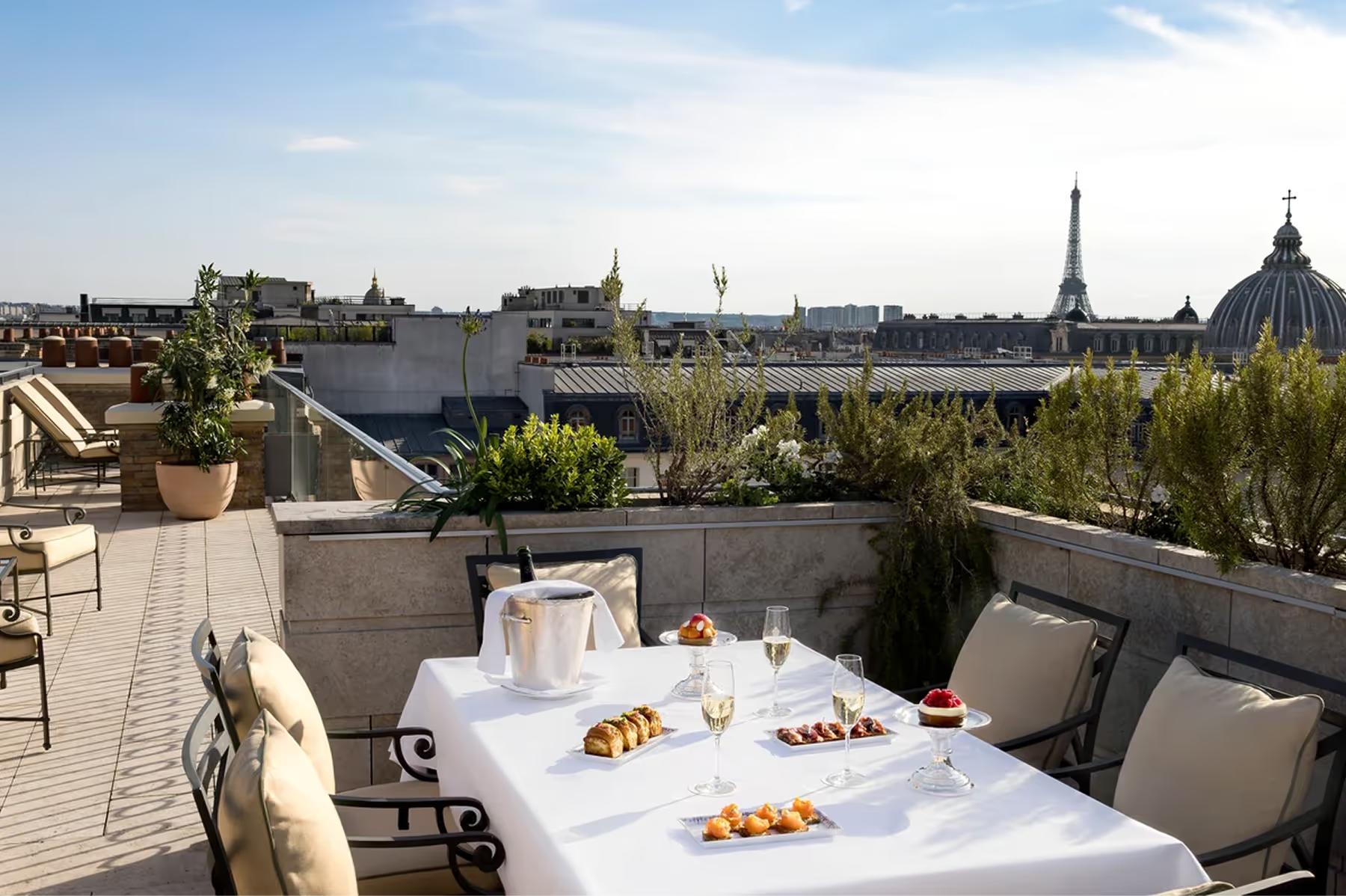 A rooftop terrace with white dining table, gray seating, and sweeping Paris skyline views