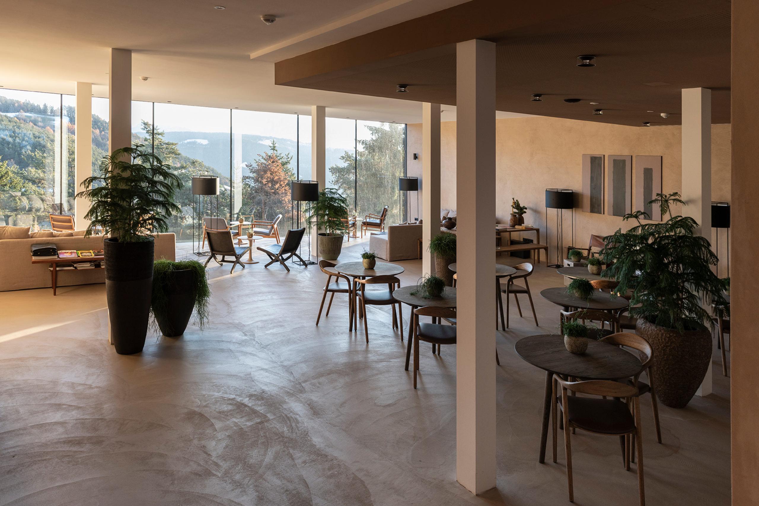 Hotel Saltus: large dining hall with concrete floor, tall support columns, and floor-to-ceiling windows overlooking mountains