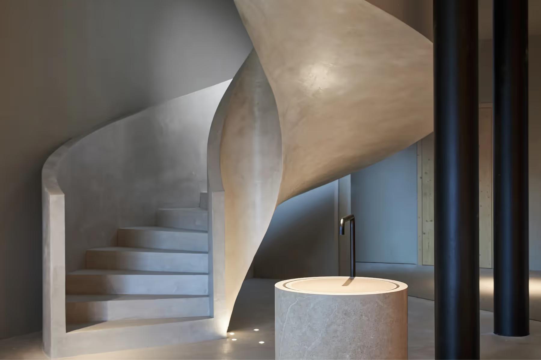 Forestis: a sculptural spiral staircase in light concrete with natural wood framing and black metal railings