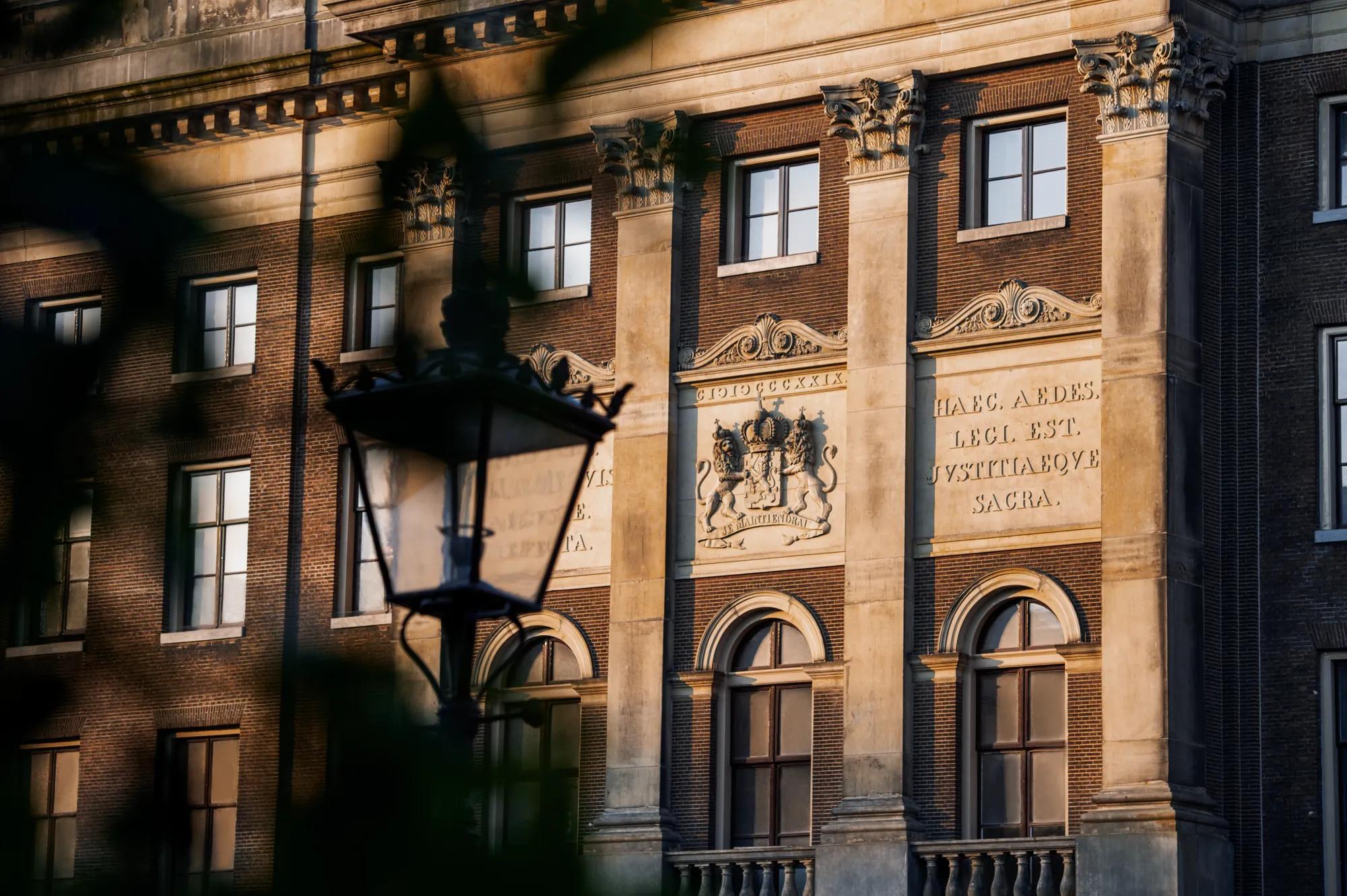 Rosewood Amsterdam: the stone facade at sunrise with the Dutch royal coat of arms and Latin inscriptions