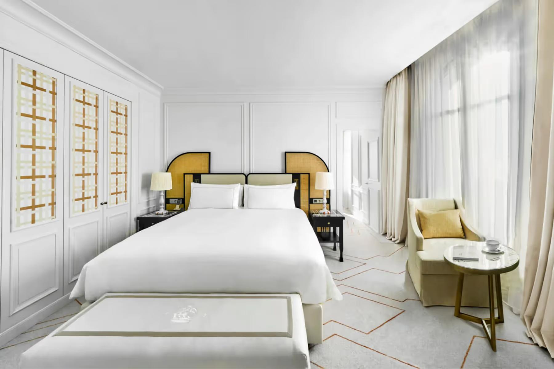Carlton Cannes: master bedroom with white bed accented by gold-trimmed nightstands, white wall paneling, and a yellow accent chair