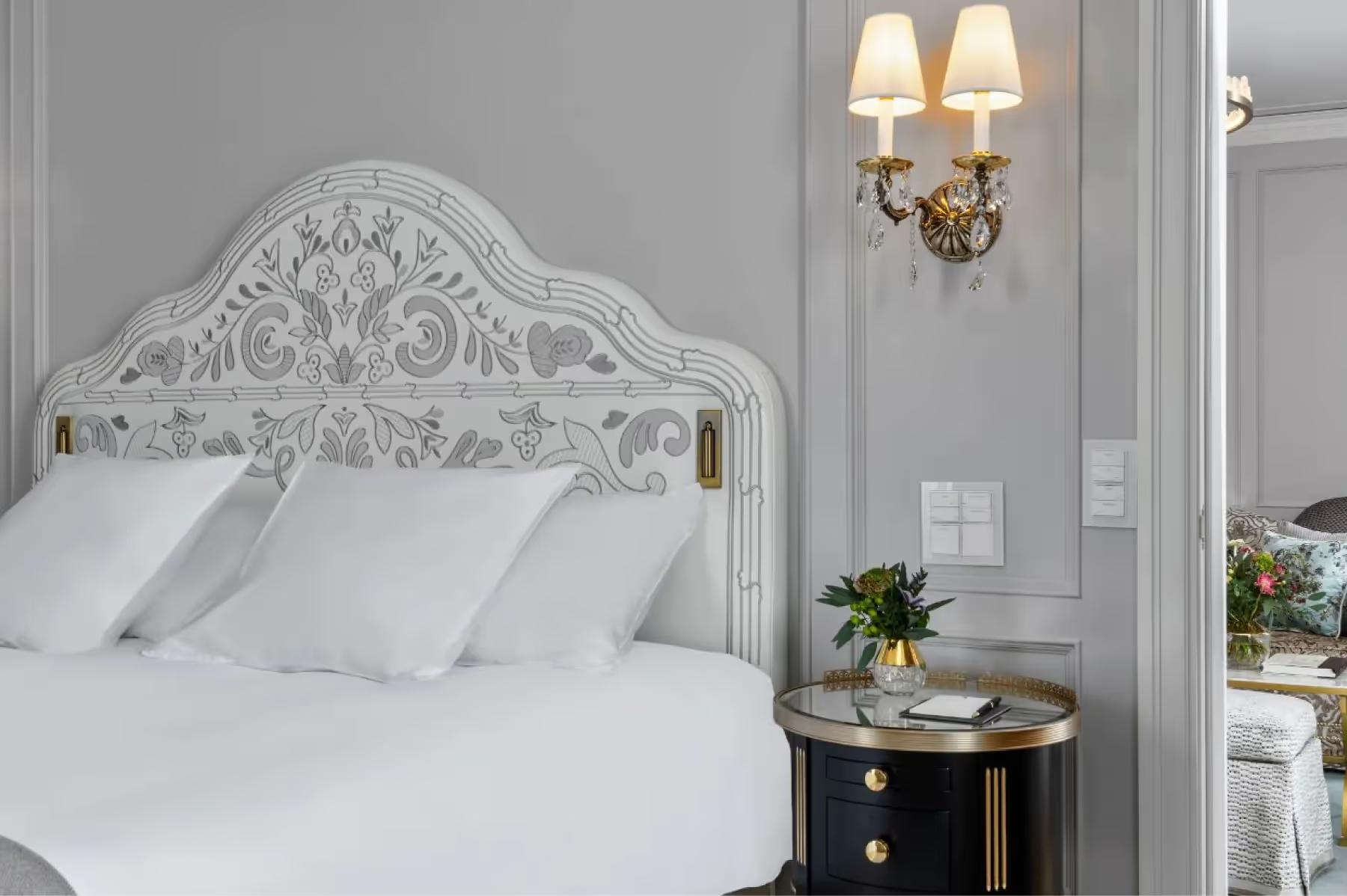 Badrutt’s Palace Hotel: bedroom with ornate white headboard, gold sconces, and bedside nightstands