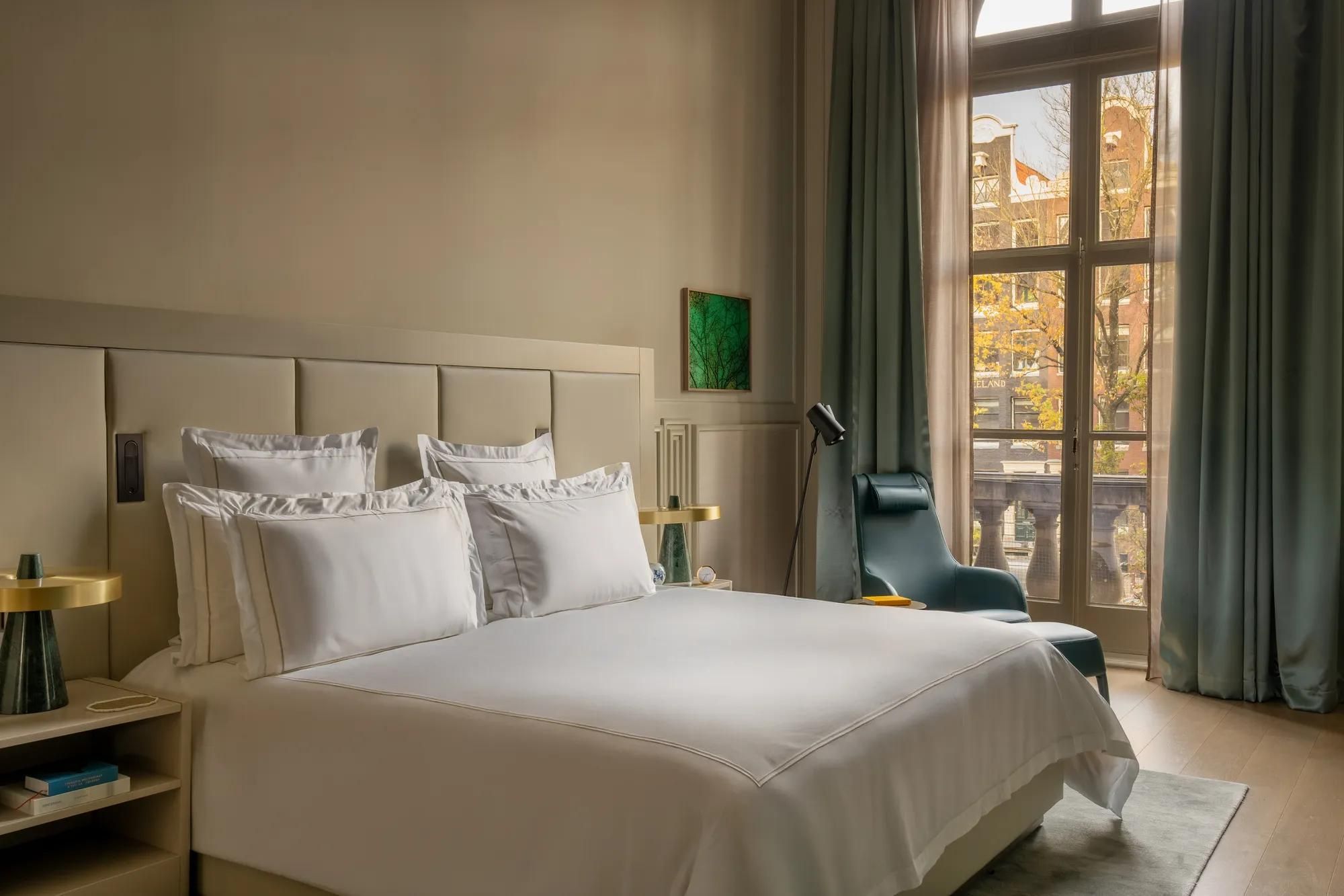 Rosewood Amsterdam: a Canal View Signature Suite bedroom with white bedding and a tall window over the canal