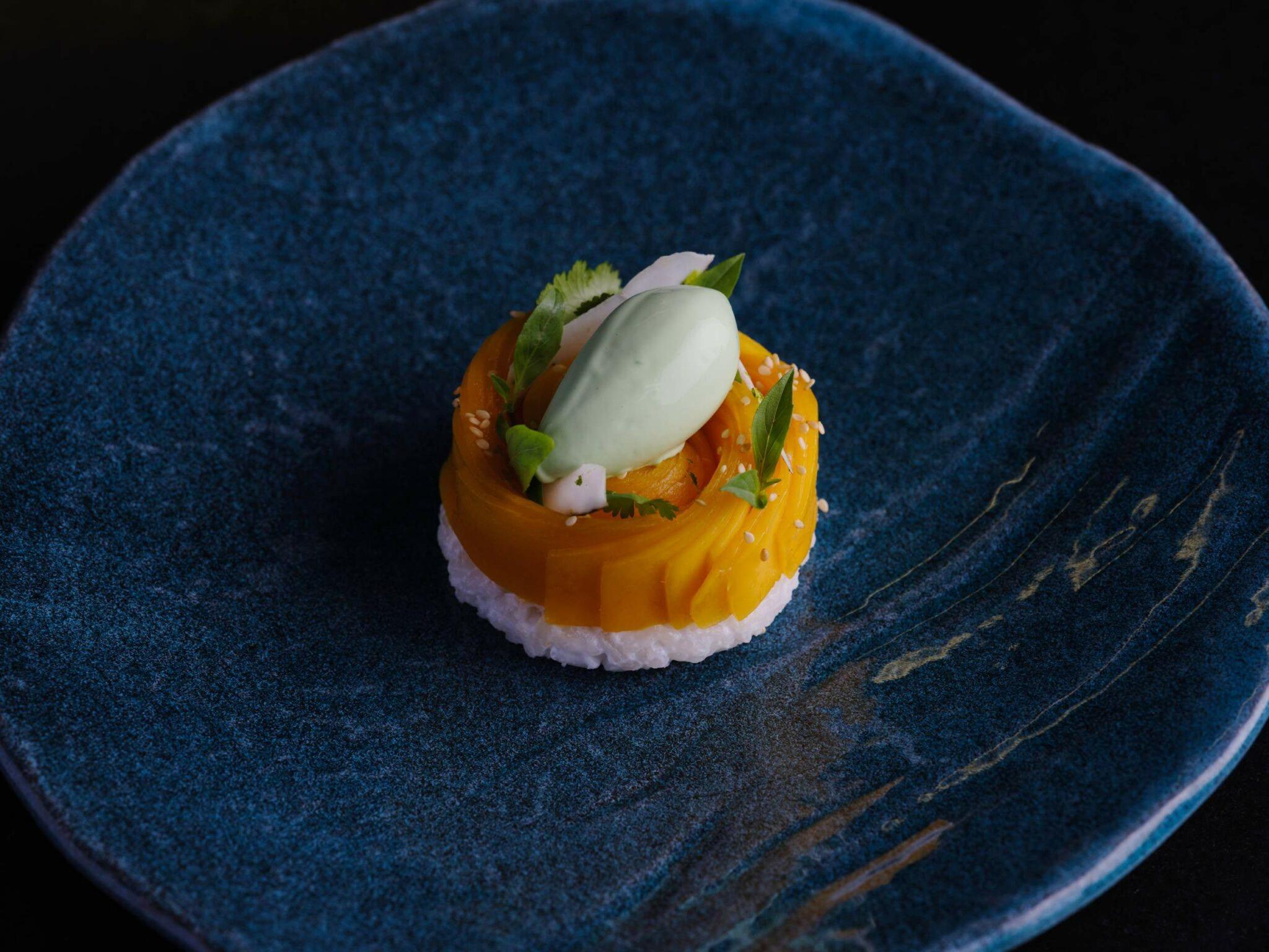 Mandarin Oriental Conservatorium, Amsterdam: dessert of thin orange fruit slices on a round of white rice, topped with a pale green scoop, on a dark blue plate