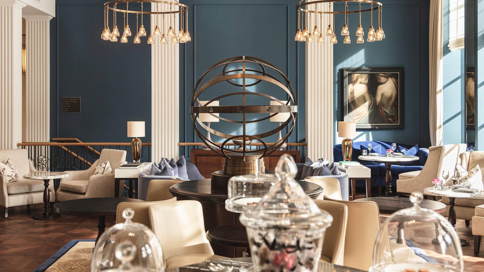 Waldorf Astoria Amsterdam: an elegant salon with blue walls, hanging gold light fixtures, marble columns, and modern sculptural art pieces