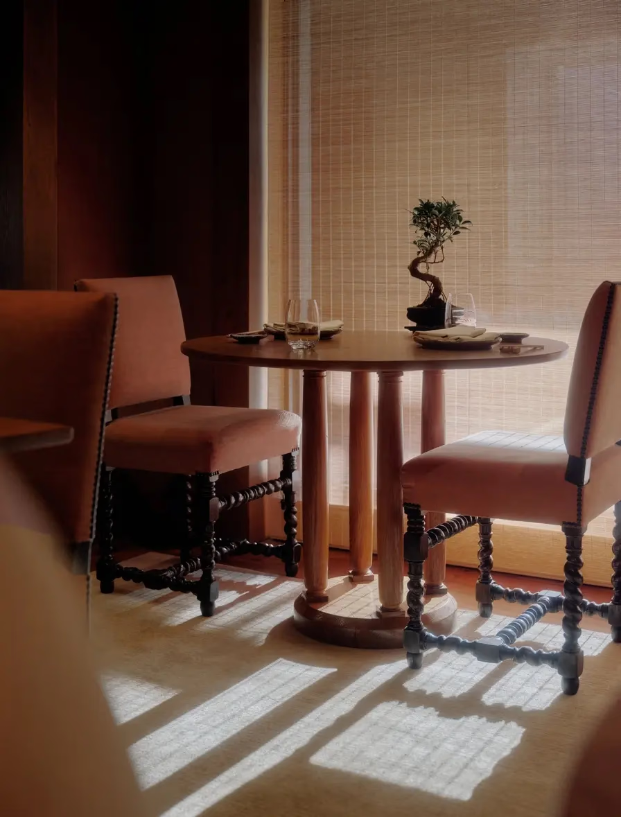 Aman Le Mélézin: table set for two with a bonsai centerpiece, terracotta chairs, and sunlight through woven blinds