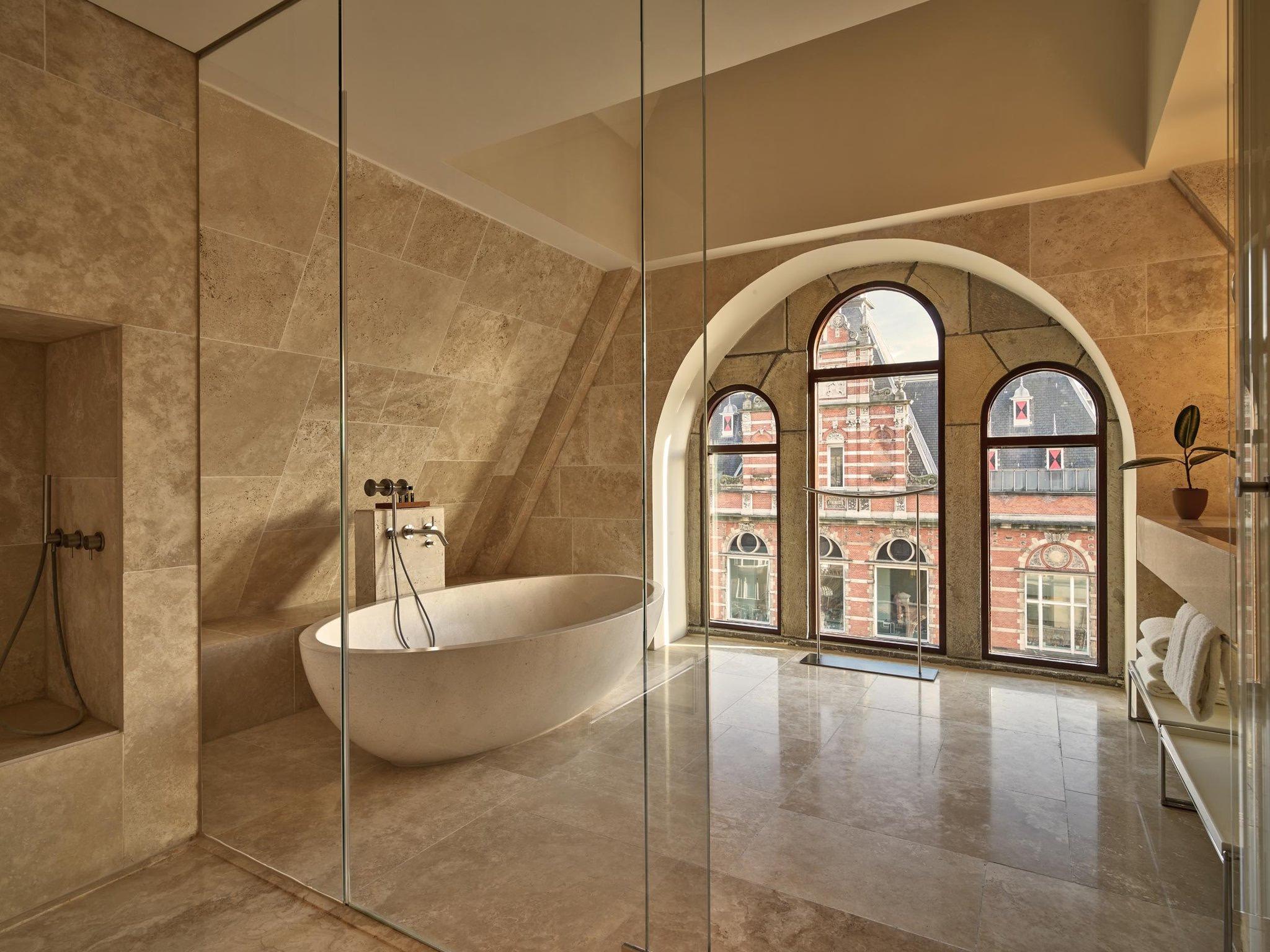 Contemporary bathroom with freestanding white soaking tub, arched windows framing city views