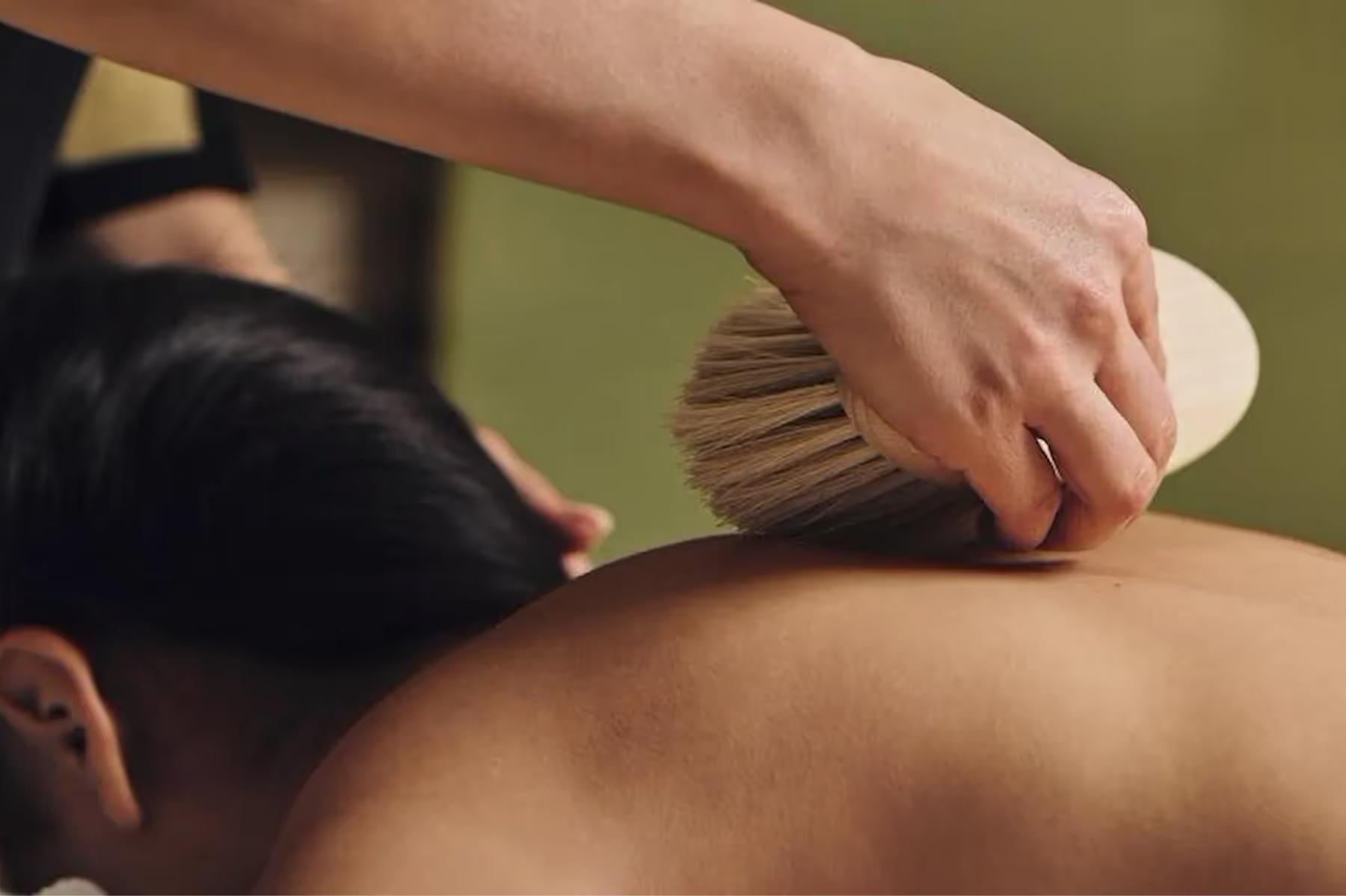 Hotel Eden: hands applying a spa massage treatment with a wooden brush on a person’s back