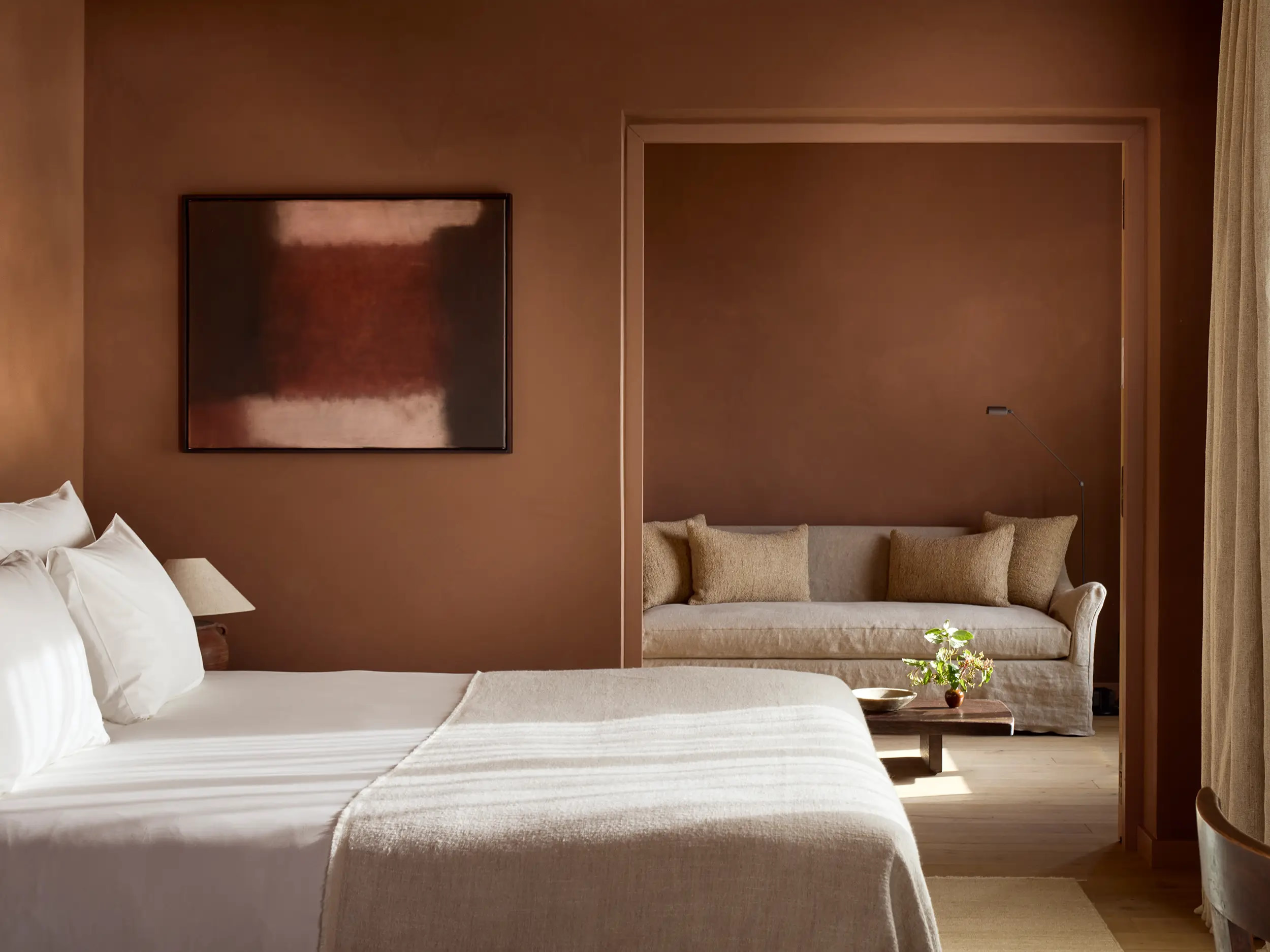 Zannier Île de Bendor: a terracotta suite pairs a framed abstract canvas with a linen sofa nook beyond the bed