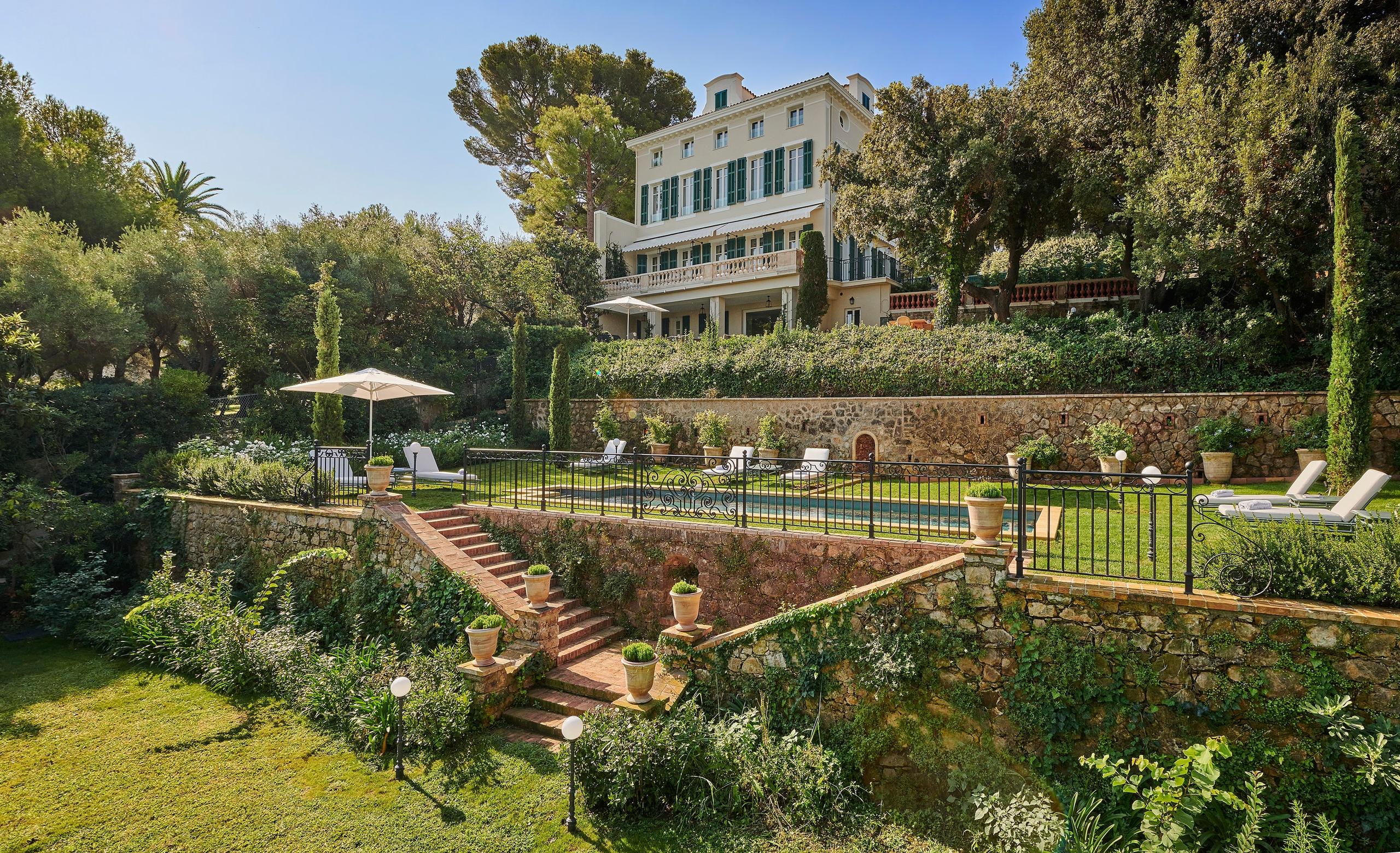 Hôtel du Cap-Eden-Roc: a poolside lounge area with cushioned seating, white umbrellas, and views of the sea and pine trees