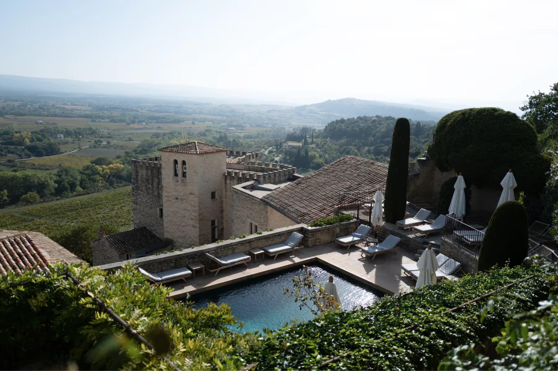 Hôtel Crillon le Brave: medieval stone buildings with turquoise pool, sun loungers under white umbrellas, boxwood hedges, and far countryside
