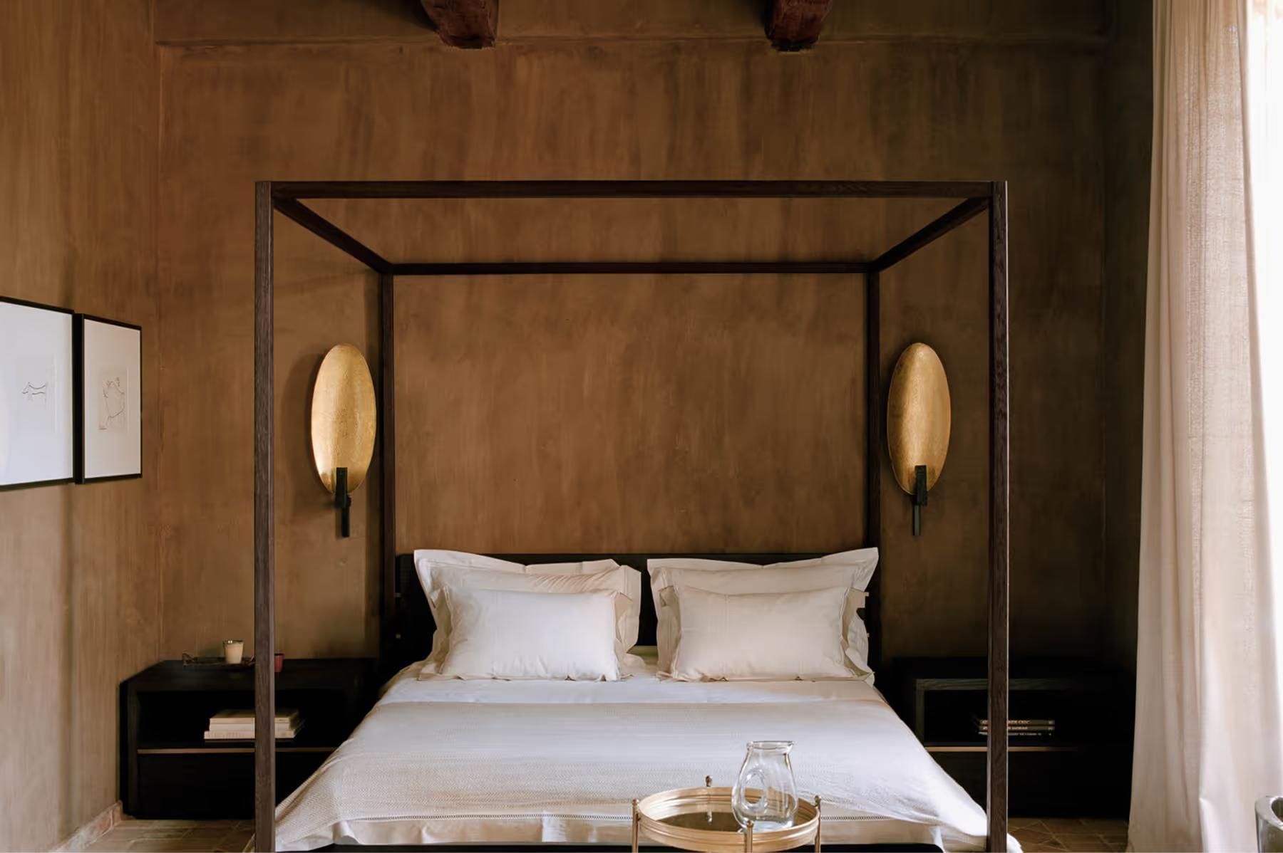 Le Mas de Chabran: canopy bed with dark wood frame and brass wall sconces in warm earth-toned room