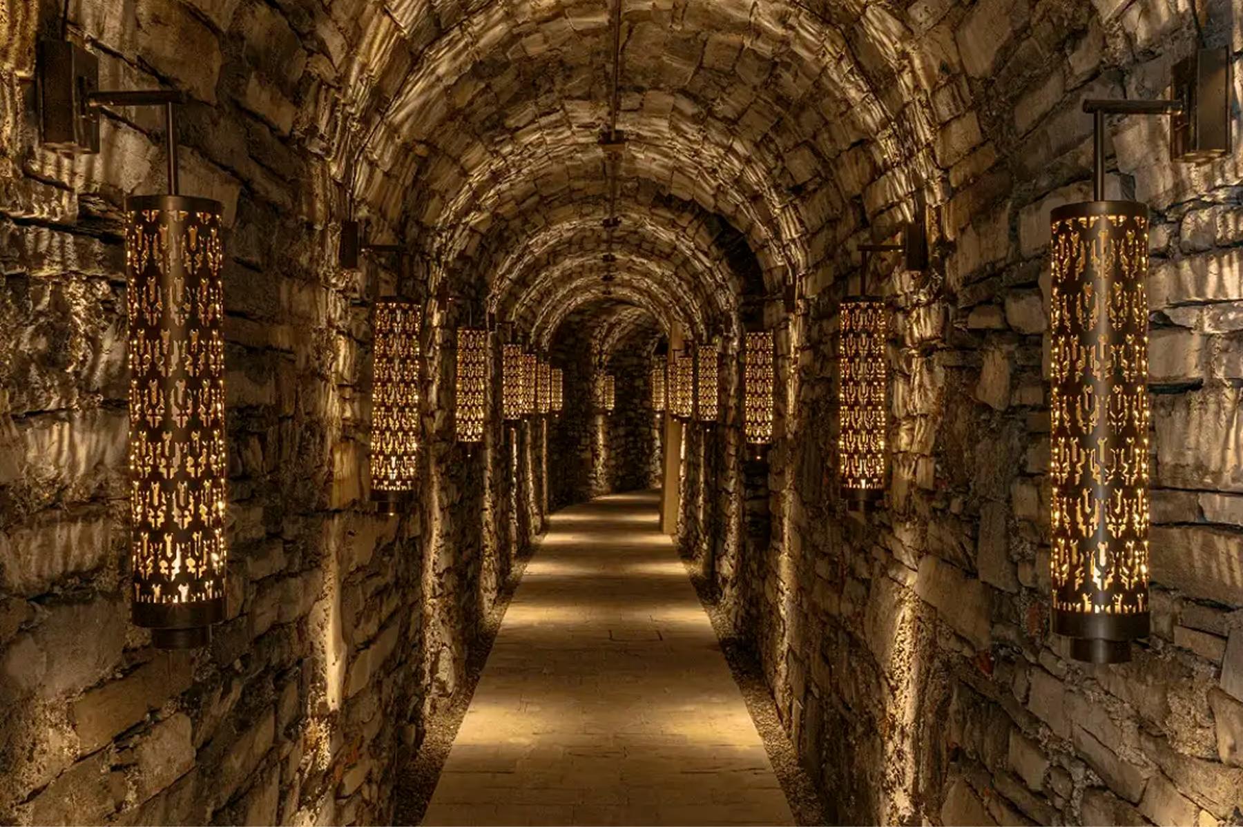 A tunnel passage with illuminated stone walls and arched brick ceiling