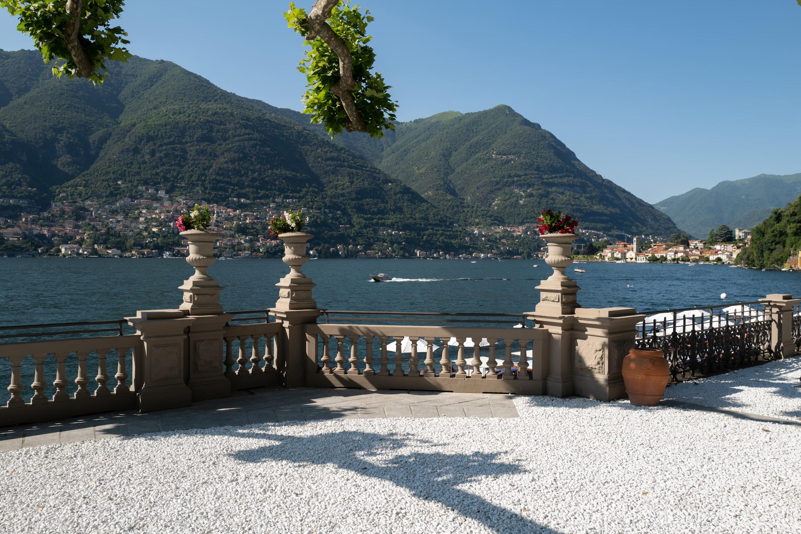 Terrace with three stone urns framing blue water, lakeside villages, and mountain vista