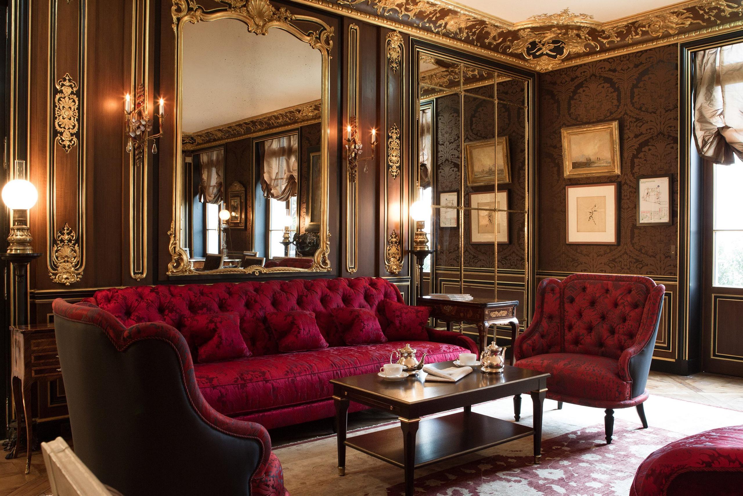 La Réserve Paris: a formal living room with burgundy seating, gold paneling, and black marble accents