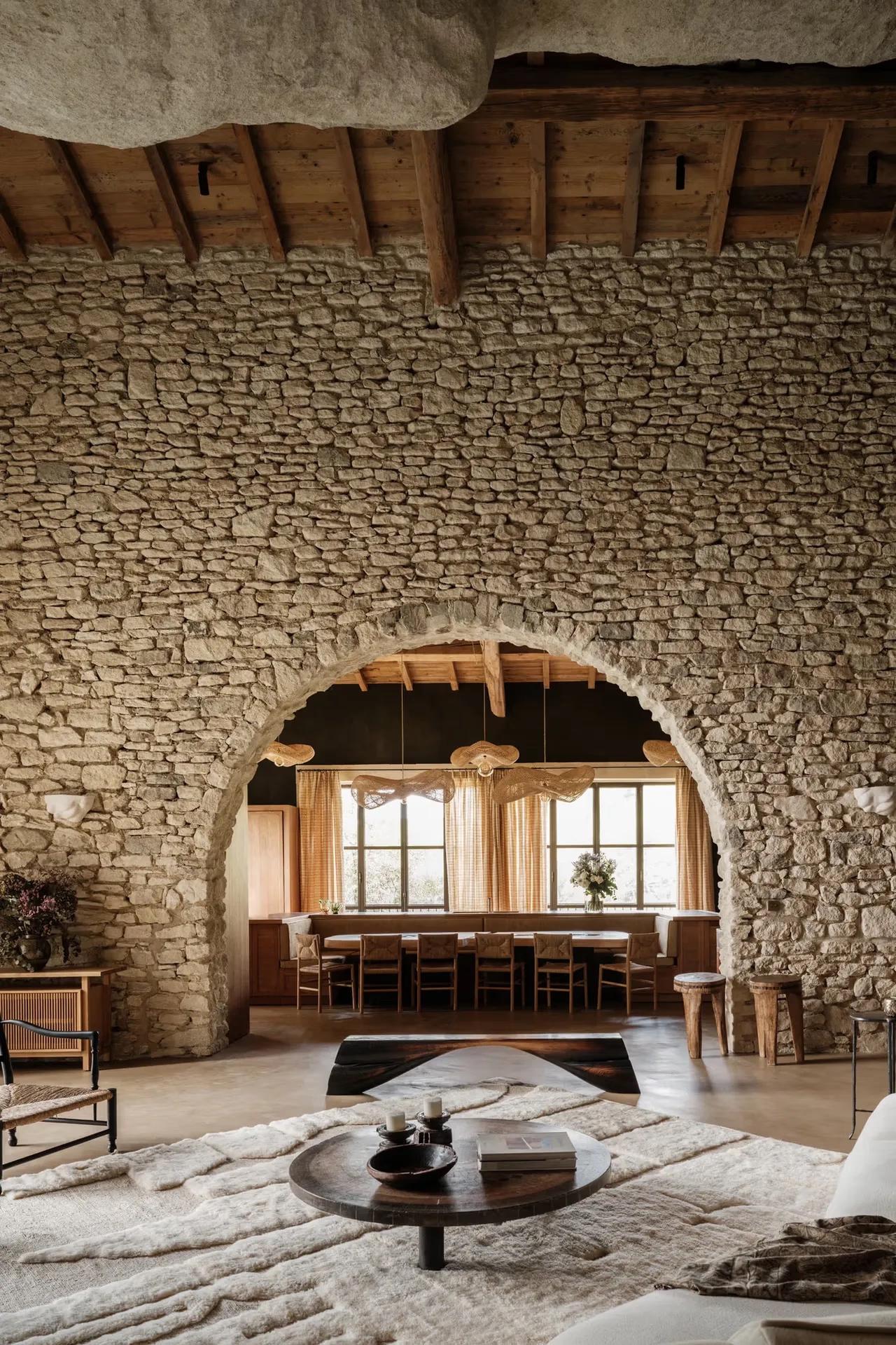 Stone archway with dark wooden lintels framing pale-draped dining room, Berber rug in foreground