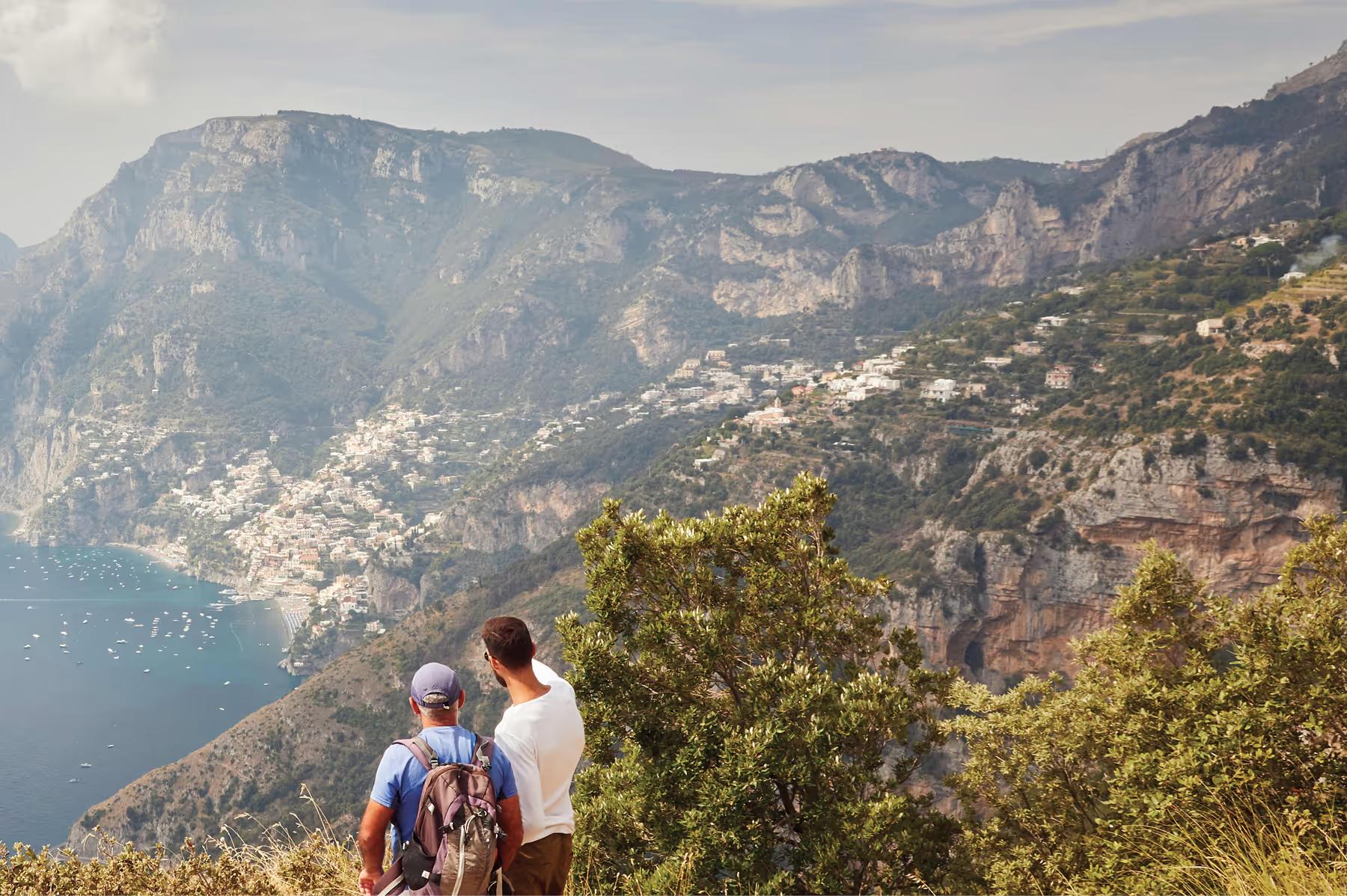 Caruso: hikers with backpacks viewing terraced coast from mountain ridge overlooking villages and blue sea