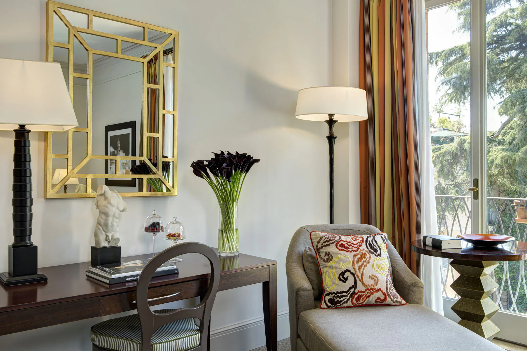 Seating area with gilt mirror, flowers, and furnishings overlooking green grounds