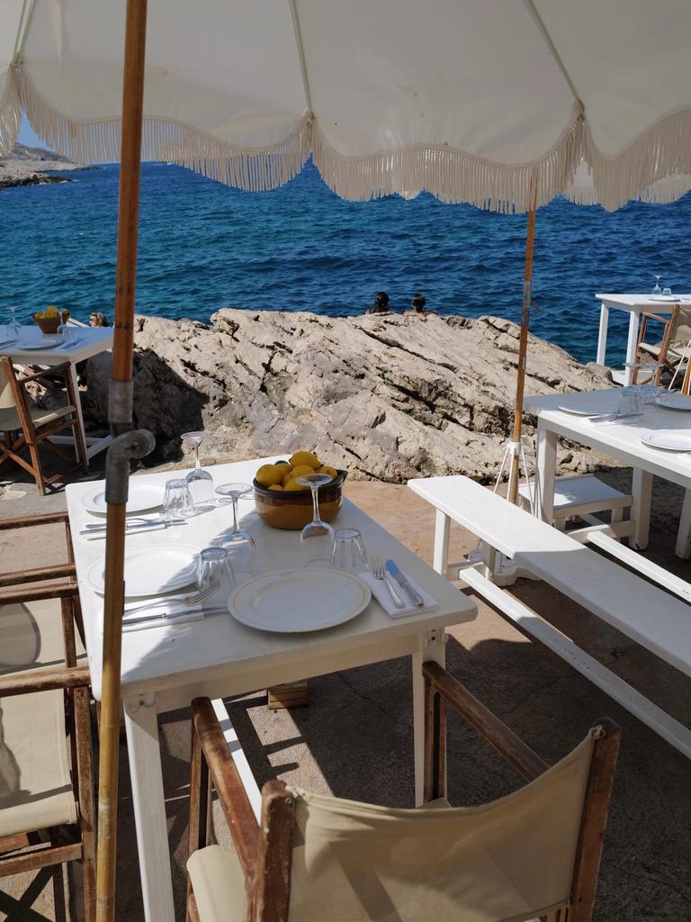 A set table under a fringed parasol at Tuba Club, the rocks and open sea beyond