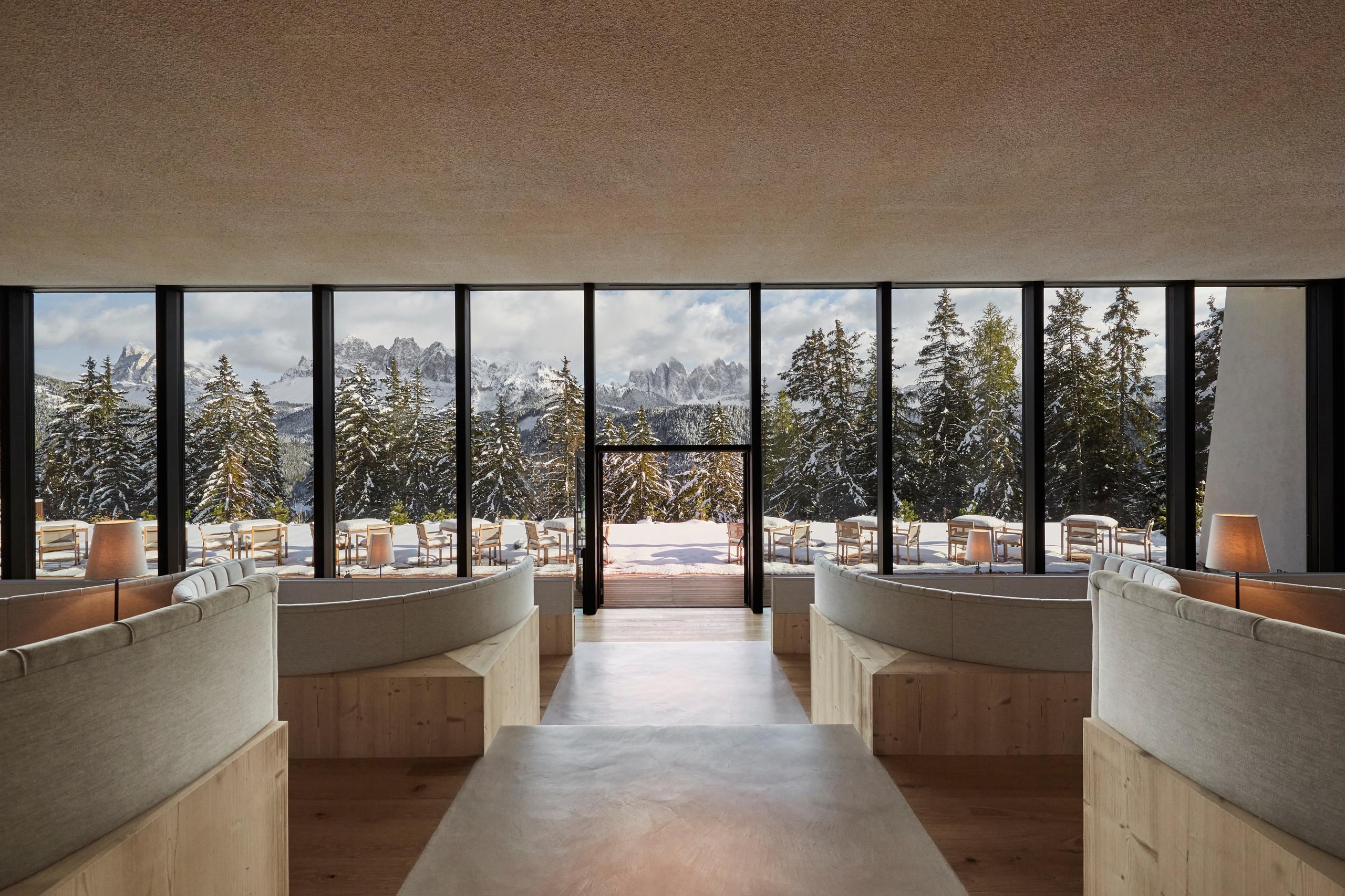 A dining room with floor-to-ceiling windows framing mountains, light wood and concrete finishes, and neutral furnishings
