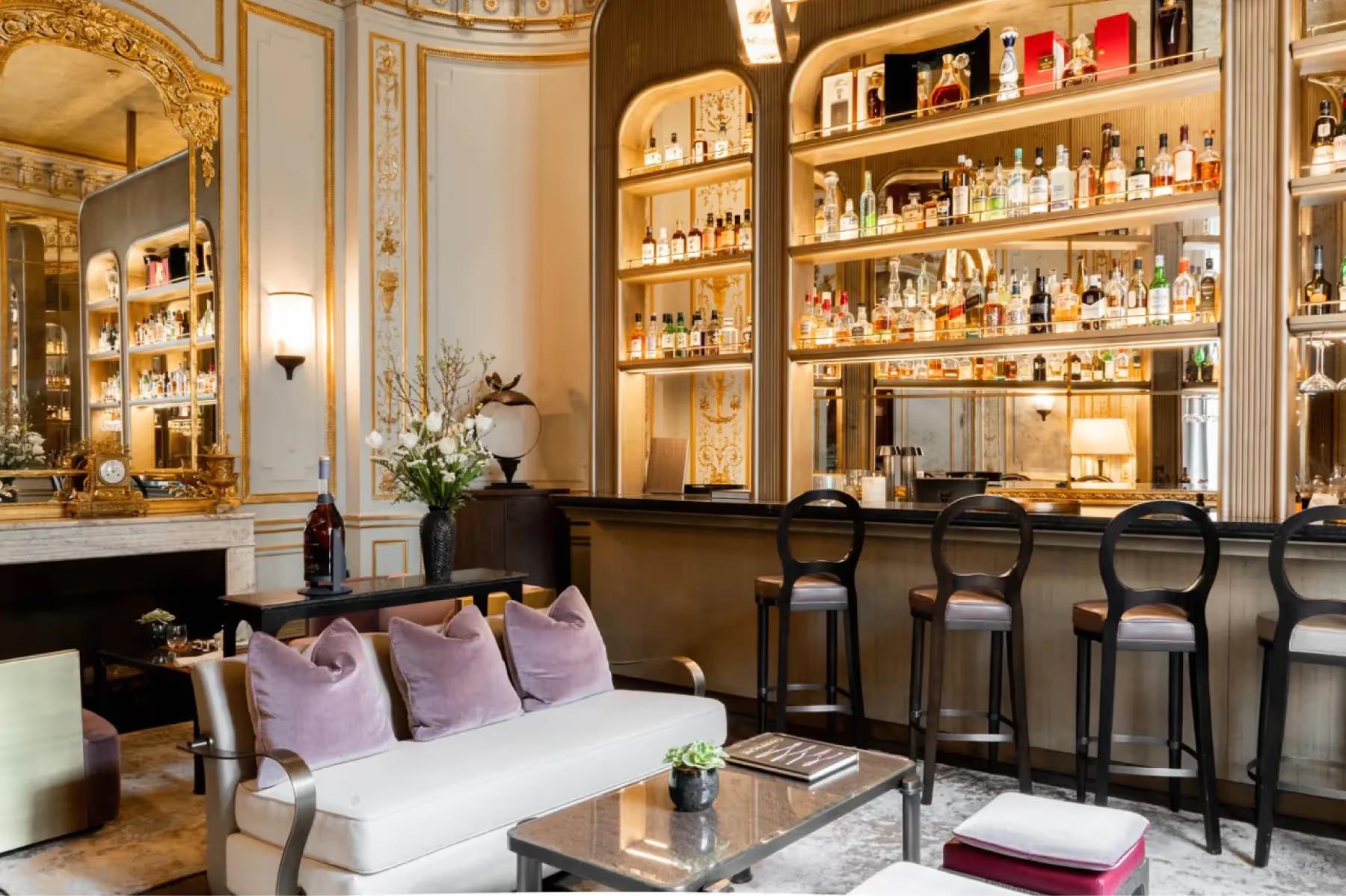 A bar lounge with illuminated glass cabinets, bar counter with stools, and ornate gold details