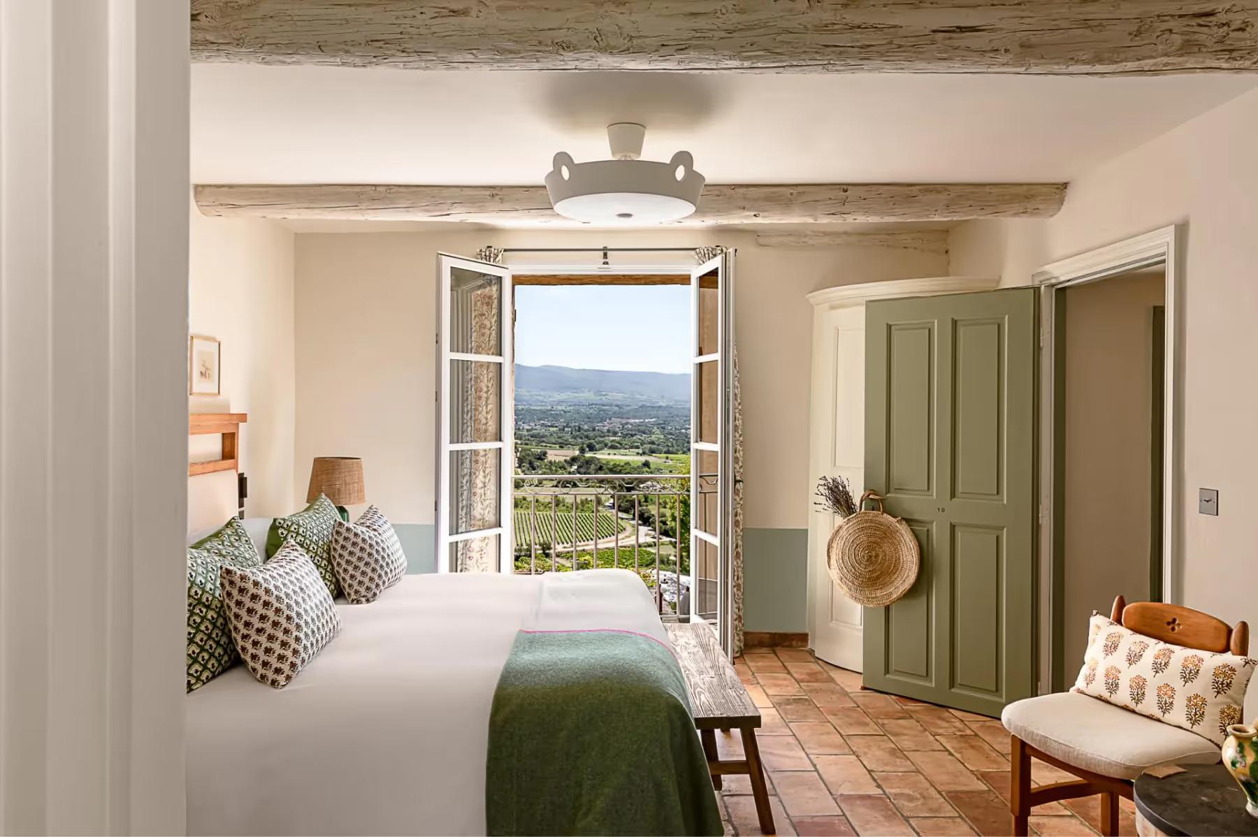 Hôtel Crillon le Brave: a bedroom with exposed wooden beams, green shutters, and an open door revealing a countryside vista