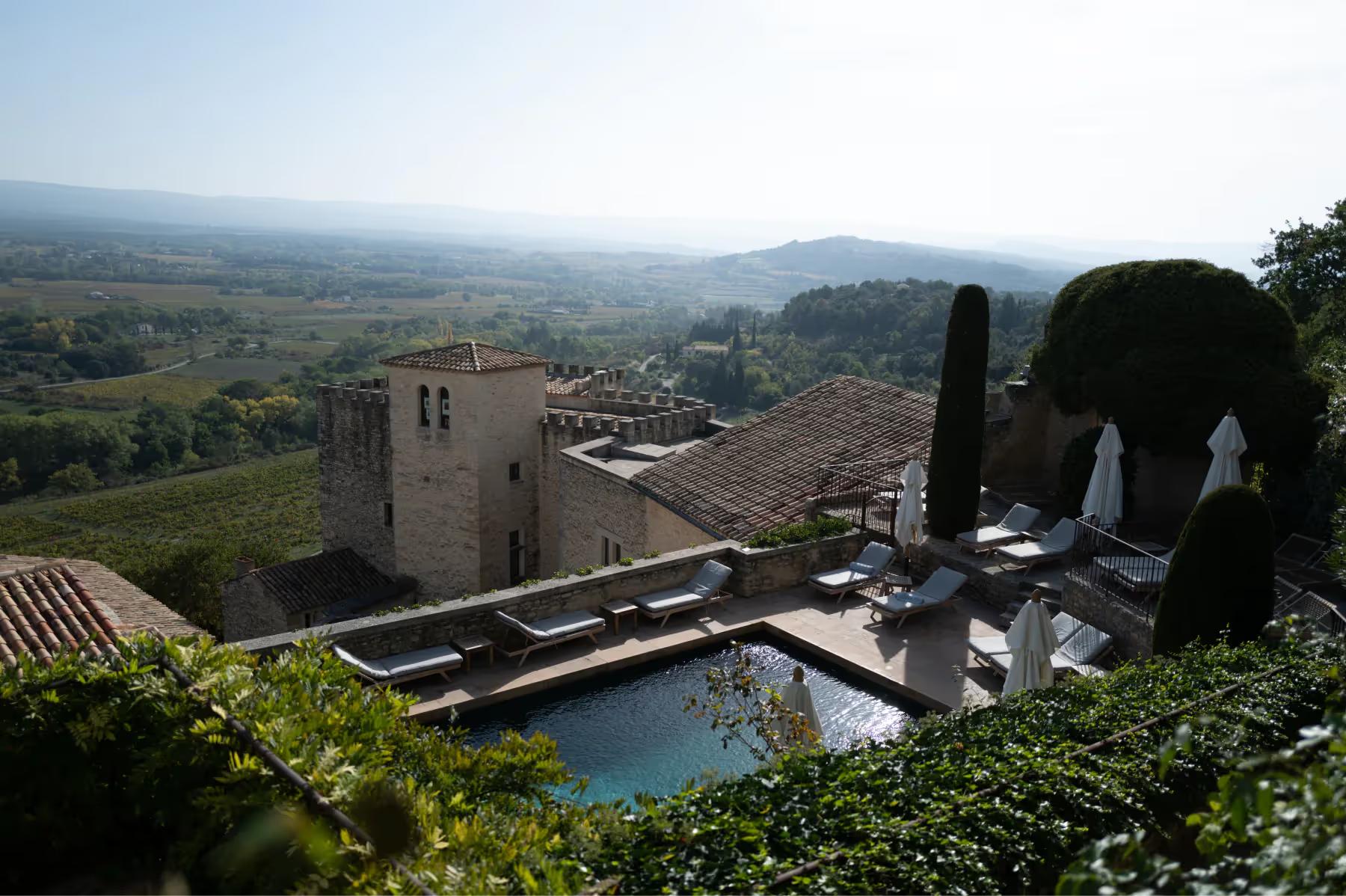 Hôtel Crillon le Brave: the hilltop village and stone buildings with a turquoise pool set below, overlooking sweeping countryside