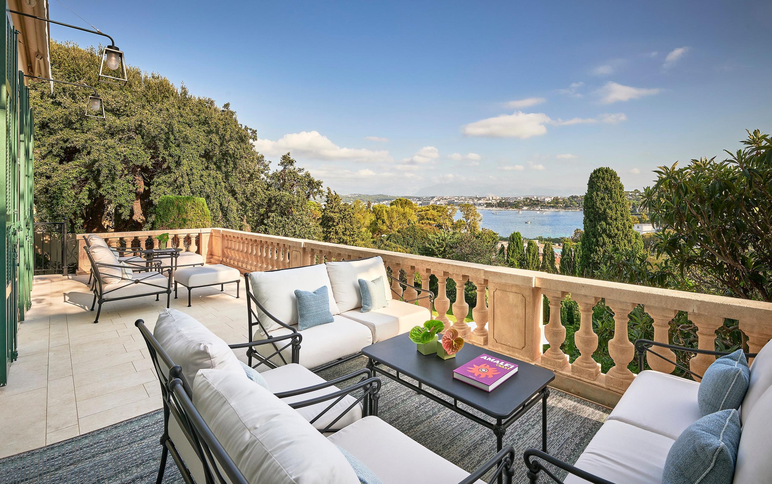 A sea-view terrace with casual seating, soft furnishings, and a stone balustrade overlooking the Mediterranean