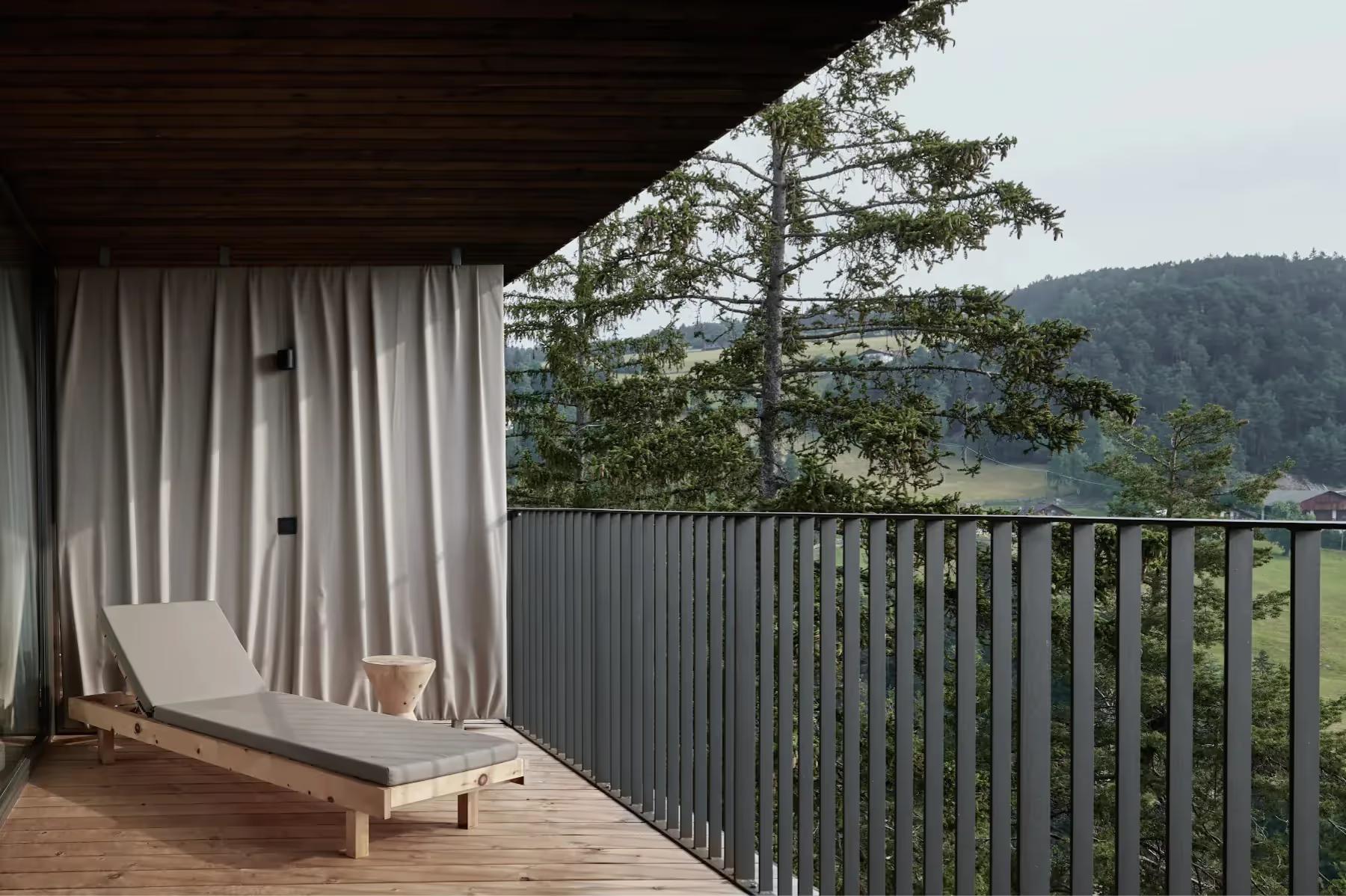 Covered wooden terrace with sheer curtains framing views of pine forest and distant mountains