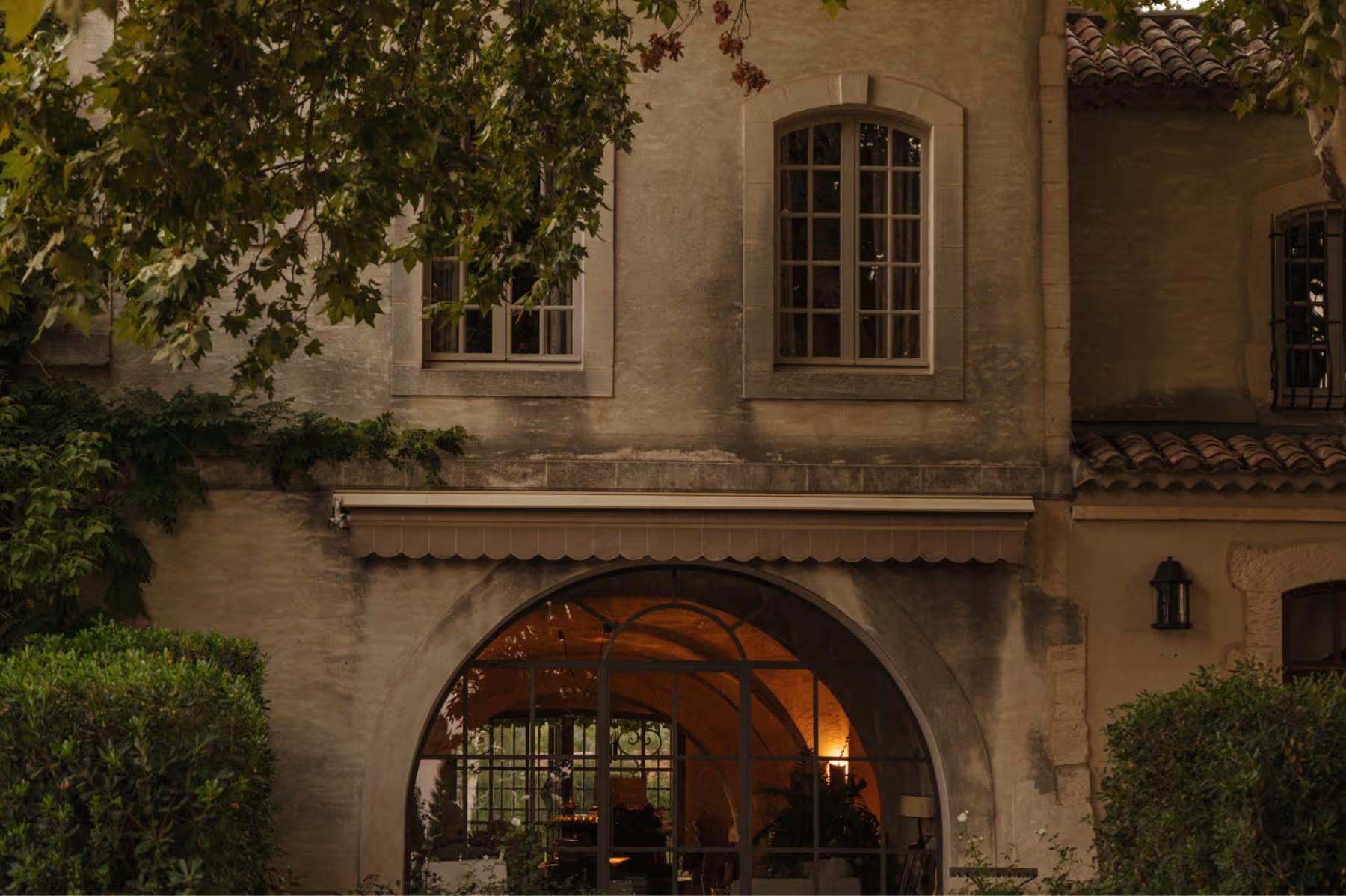 Stone facade with arched entry glowing from warm interior light at evening