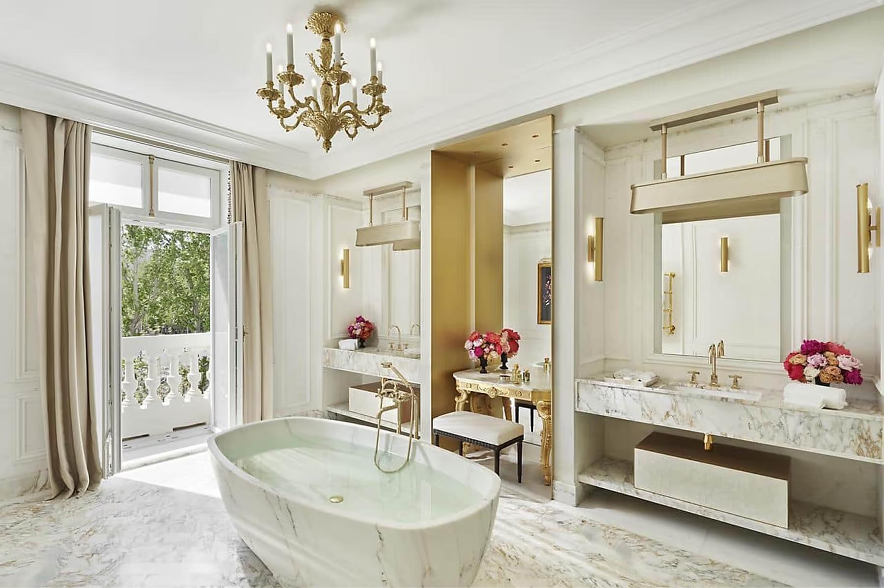 Spa bathroom with marble tub, chandelier, and floral table arrangements