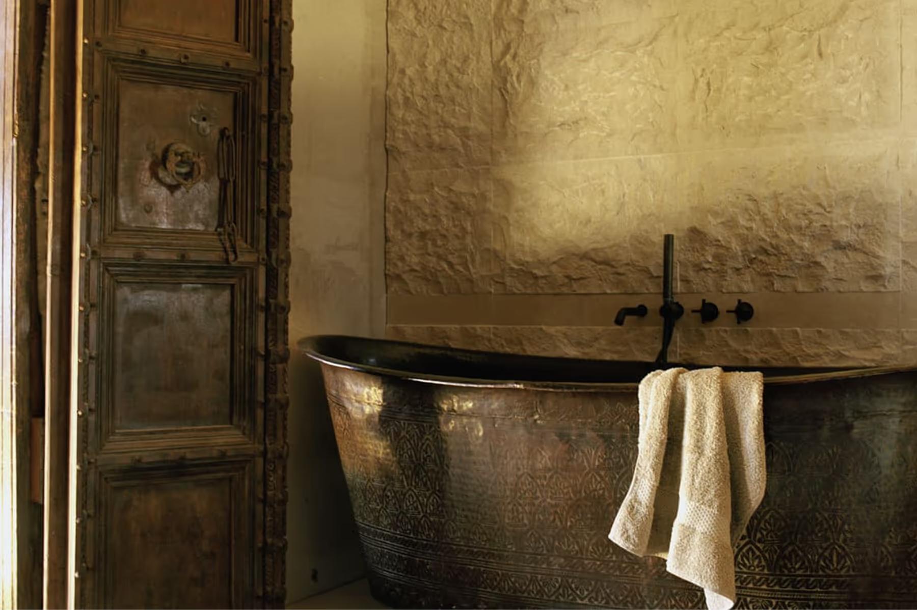 Stone bathroom with antiqued metal freestanding tub and weathered plaster walls