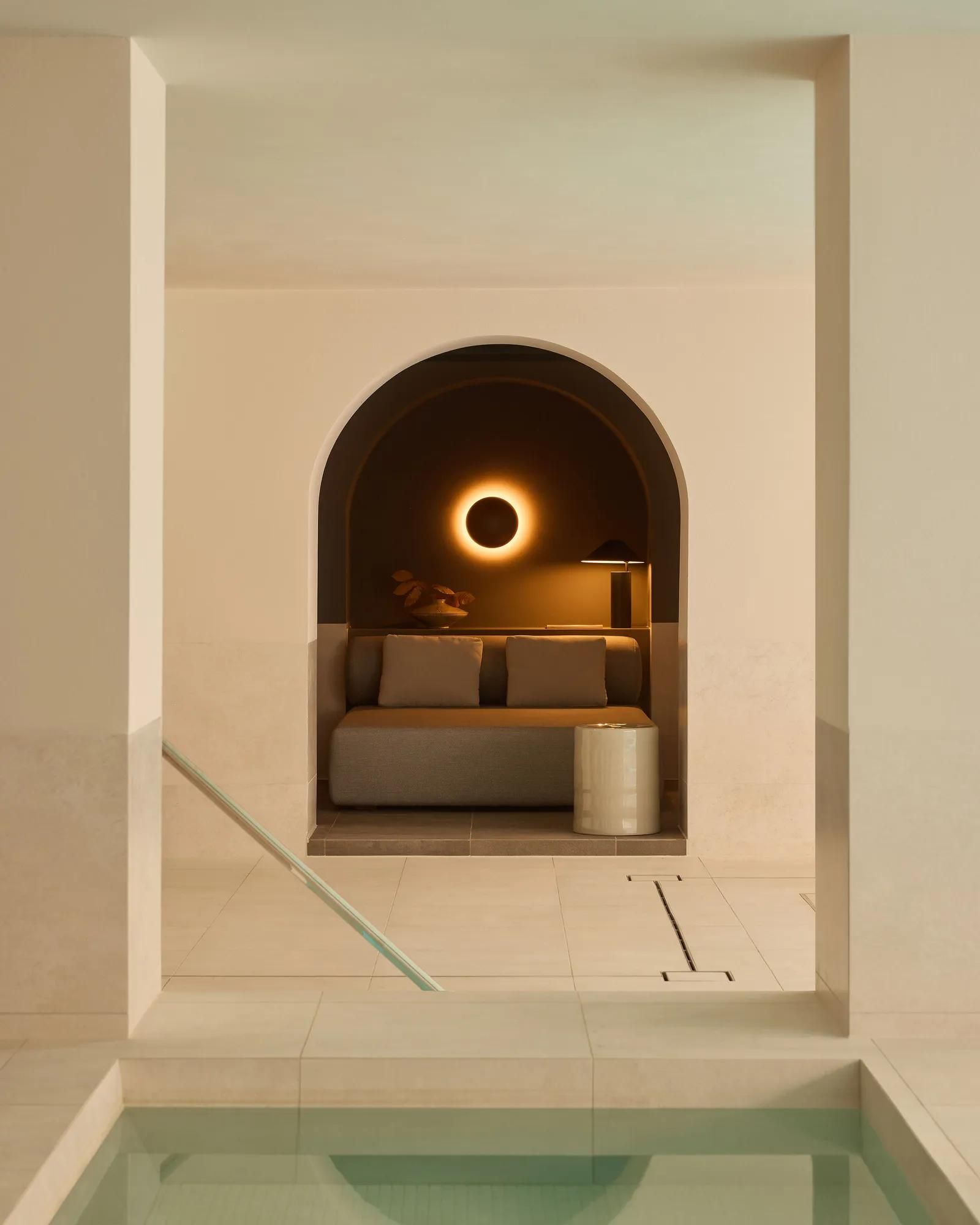 Rosewood Amsterdam: an arched alcove with a cushioned bench and a round wall light beside the Asaya pool