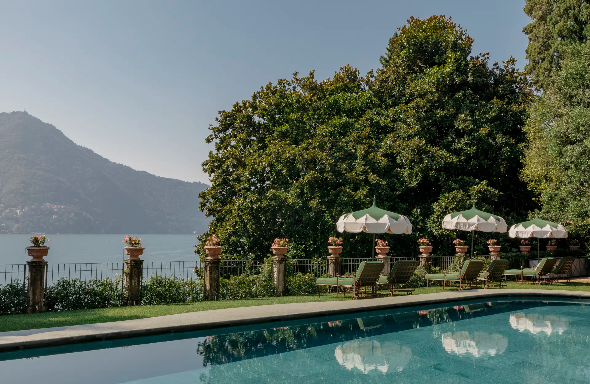 A rectangular pool reflecting cypress trees with Lake Como and mountains in the distance