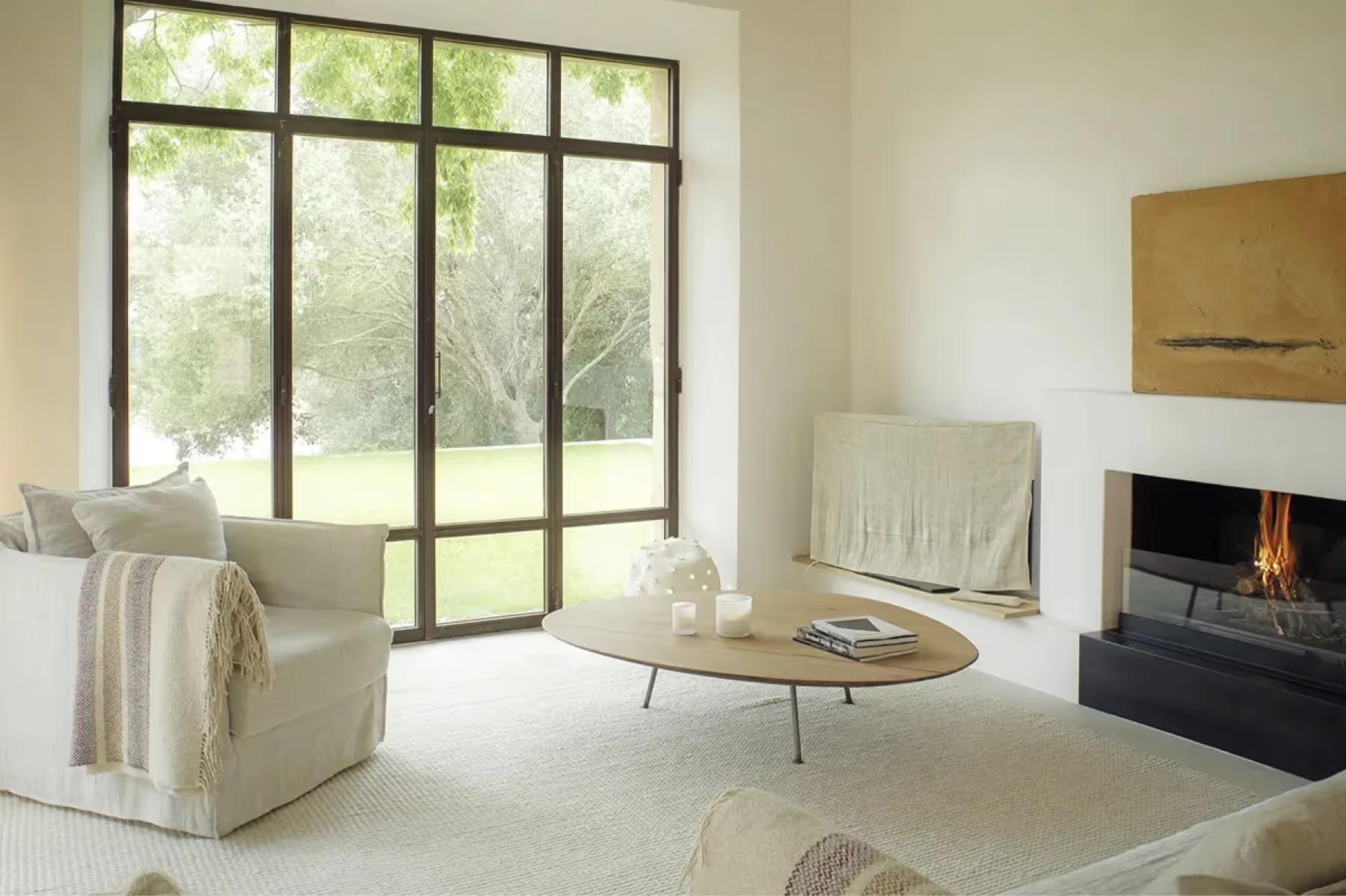 Es Racó d’Artà: contemporary living room with fireplace, metal-framed door wall opening to grounds, and light-toned furnishings
