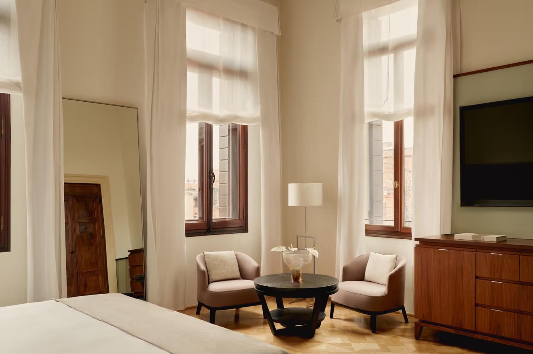 Aman Venice: a room corner with high ceilings, tall windows, brown leather seating, and wooden flooring in warm tones