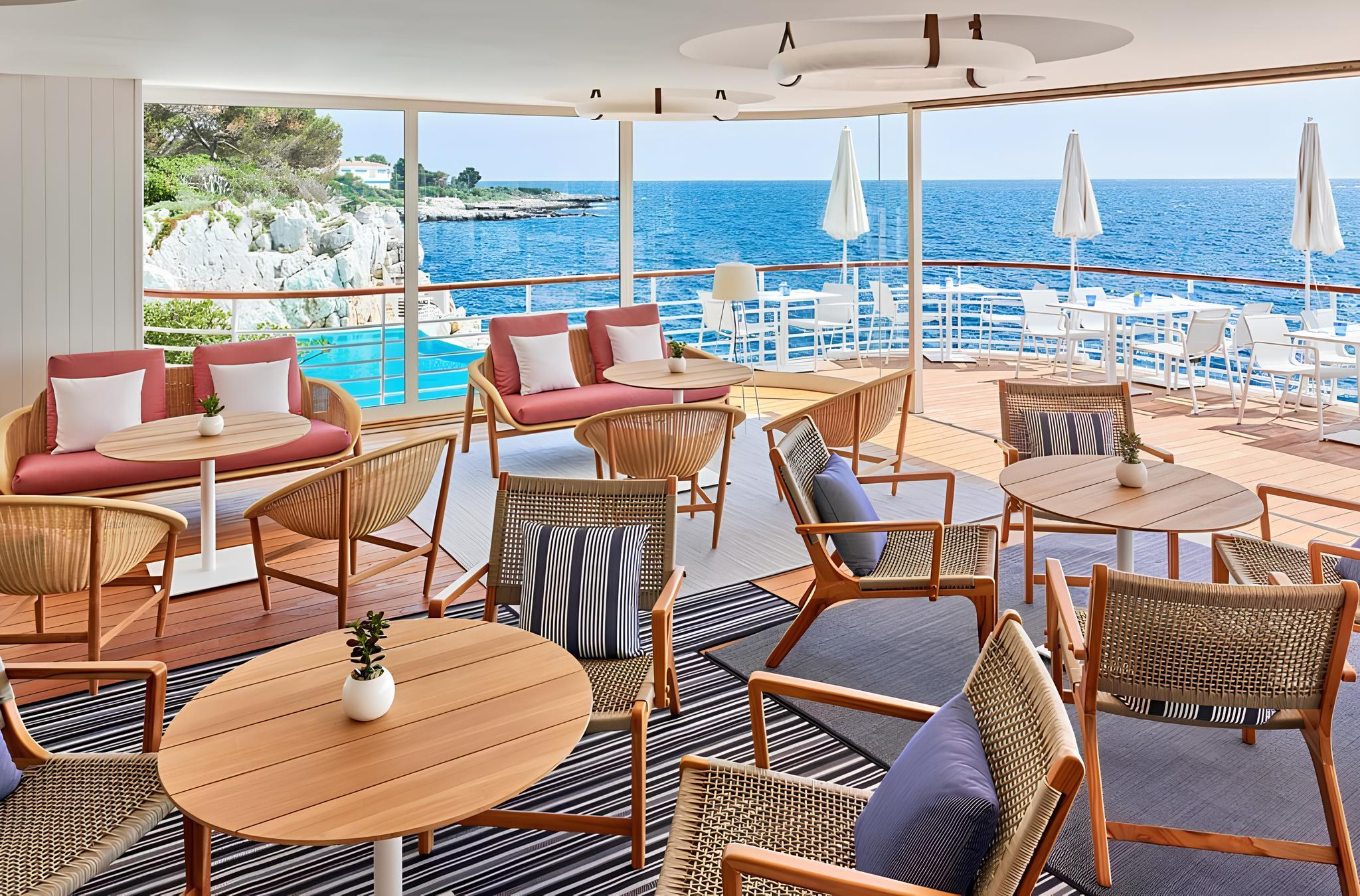 Hôtel du Cap-Eden-Roc: an indoor dining room with cream seating, glass chandelier, arched architecture, and sea vistas