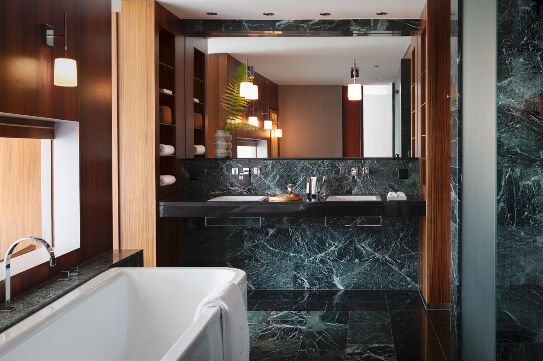 Chenot Palace Weggis: luxury bathroom with dark marble, freestanding tub, wood accents, and illuminated mirror