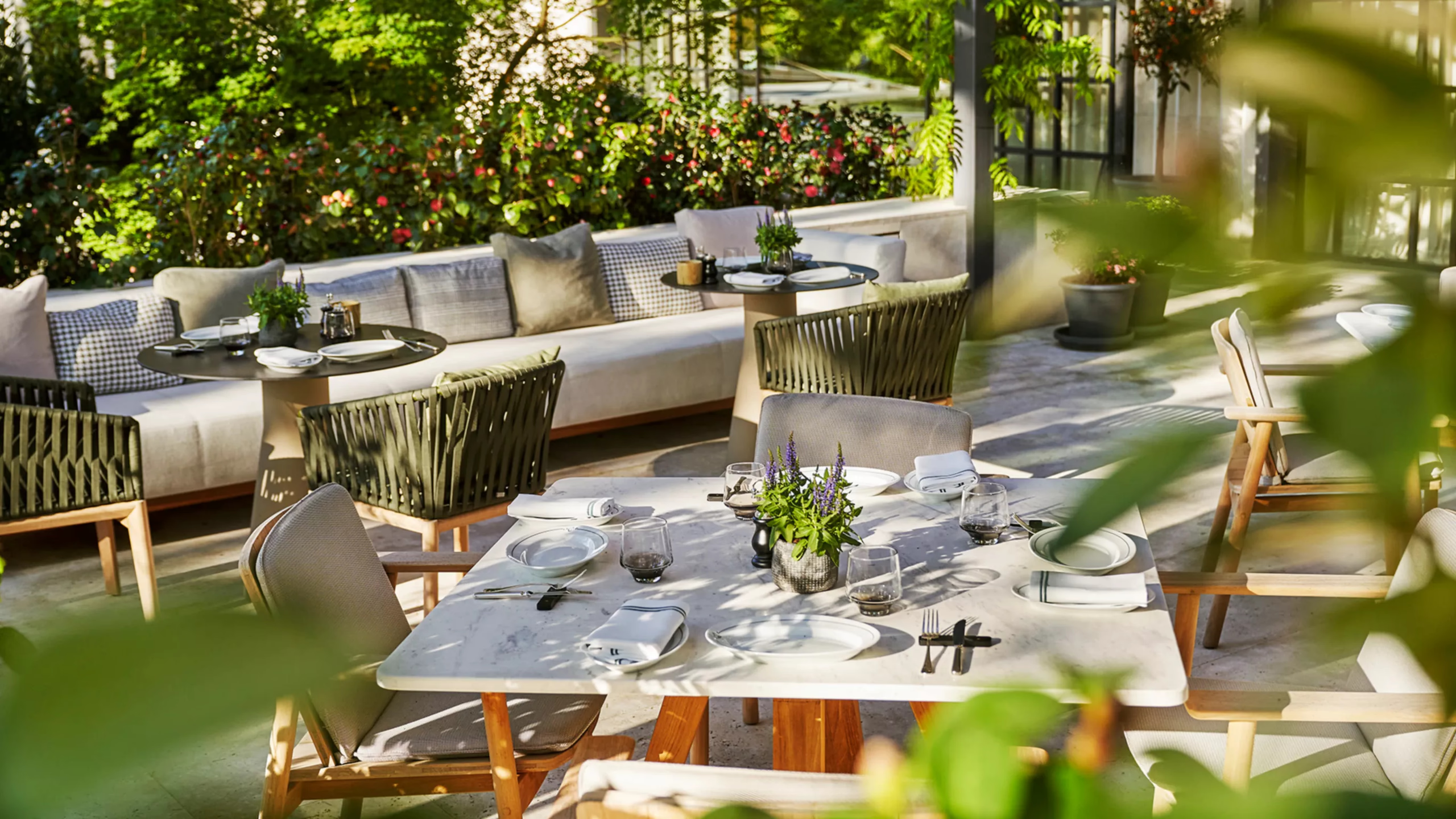 An outdoor courtyard with green seating, tables set for dining, and lush plants in foreground