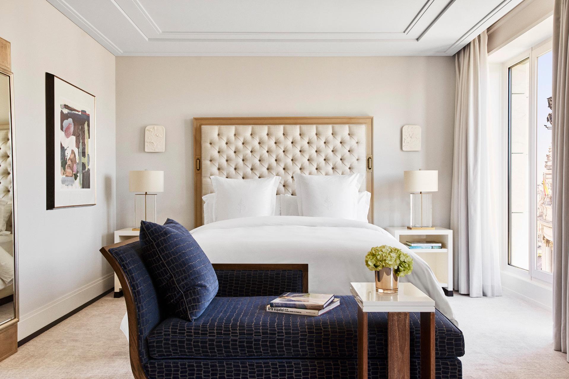 Four Seasons Hotel Madrid: suite bedroom with quilted white headboard, blue accent chair, and French doors with cream curtains