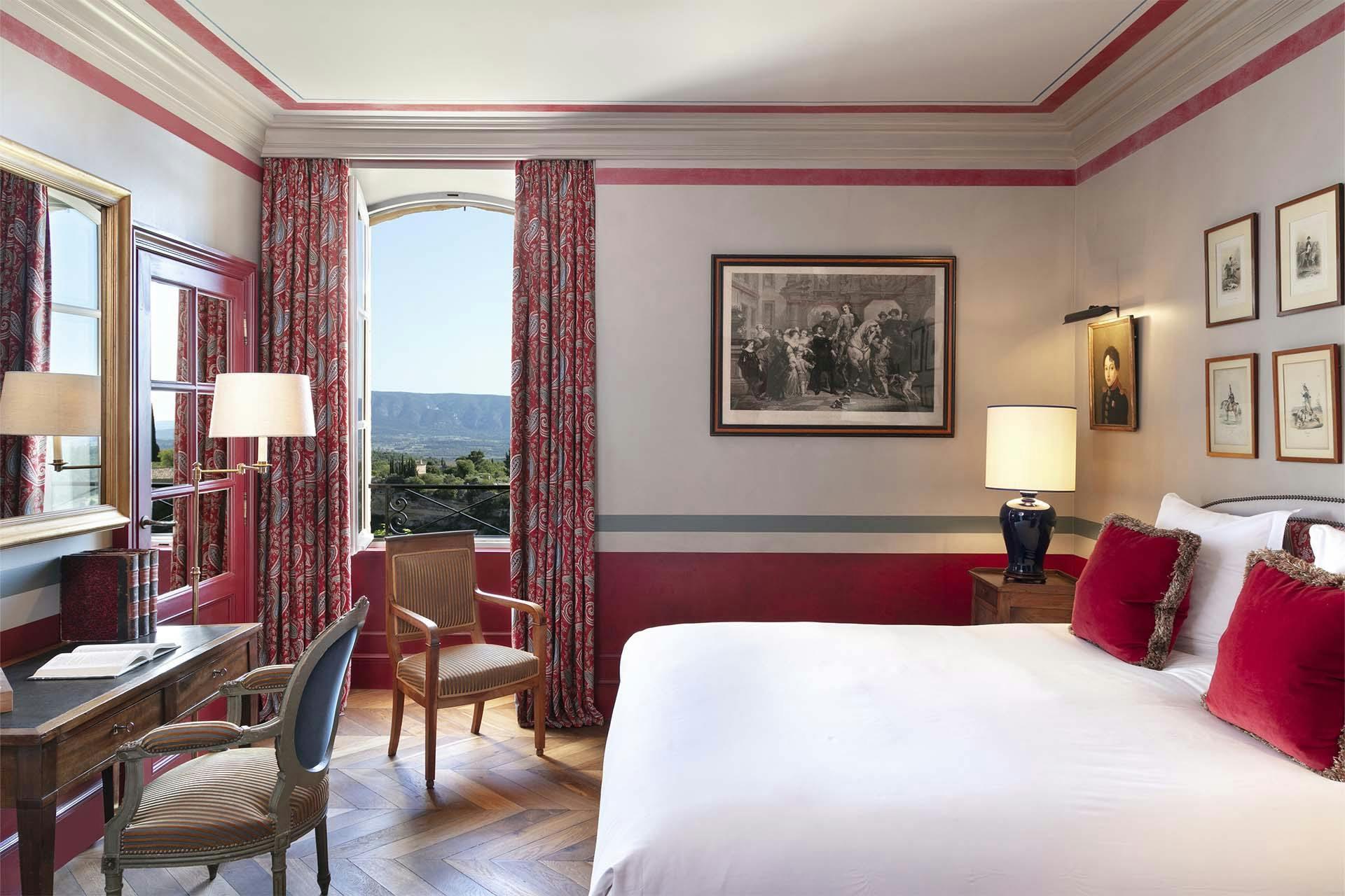 Airelles Gordes, La Bastide: bedroom with burgundy trim, draped curtains, white bedding, and valley views through French doors