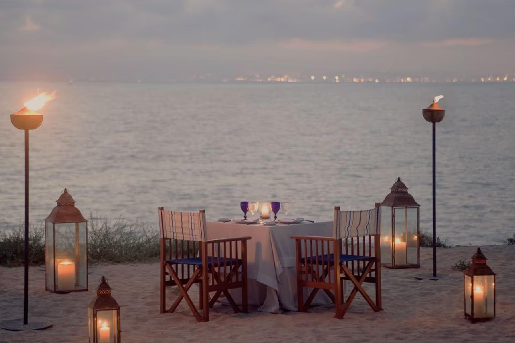 A terrace dining setting at twilight with wooden chairs, candlelit table, and bay views