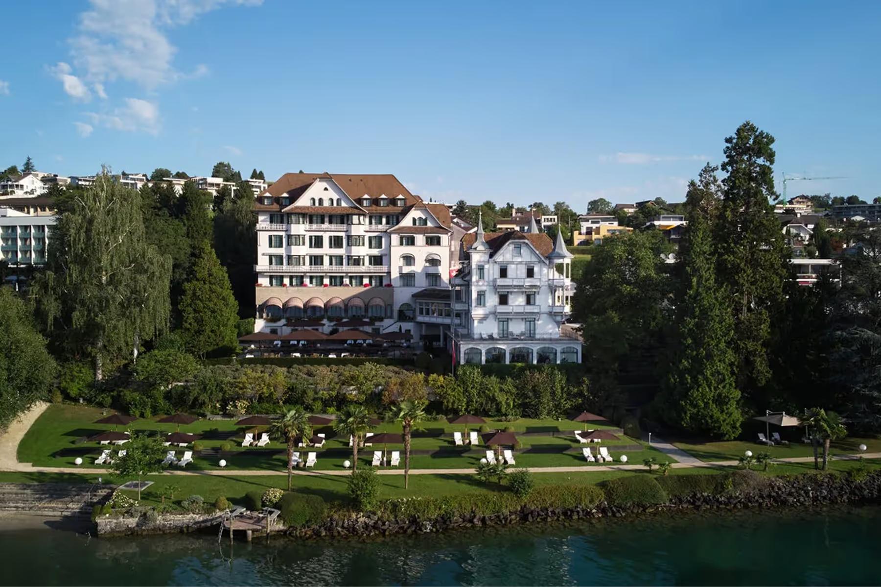 Whitewashed hotel building with turret beside Lake Lucerne, surrounded by mature trees