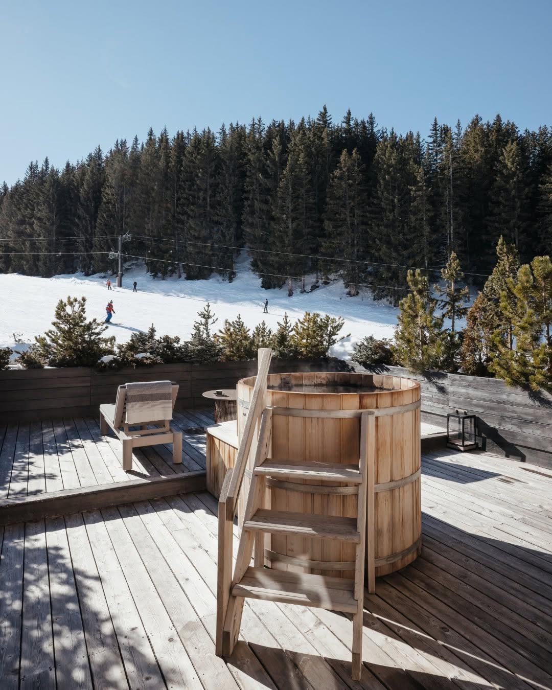 Aman Le Mélézin: wood barrel hot tub steaming on a deck above the piste and snow laden pine forest