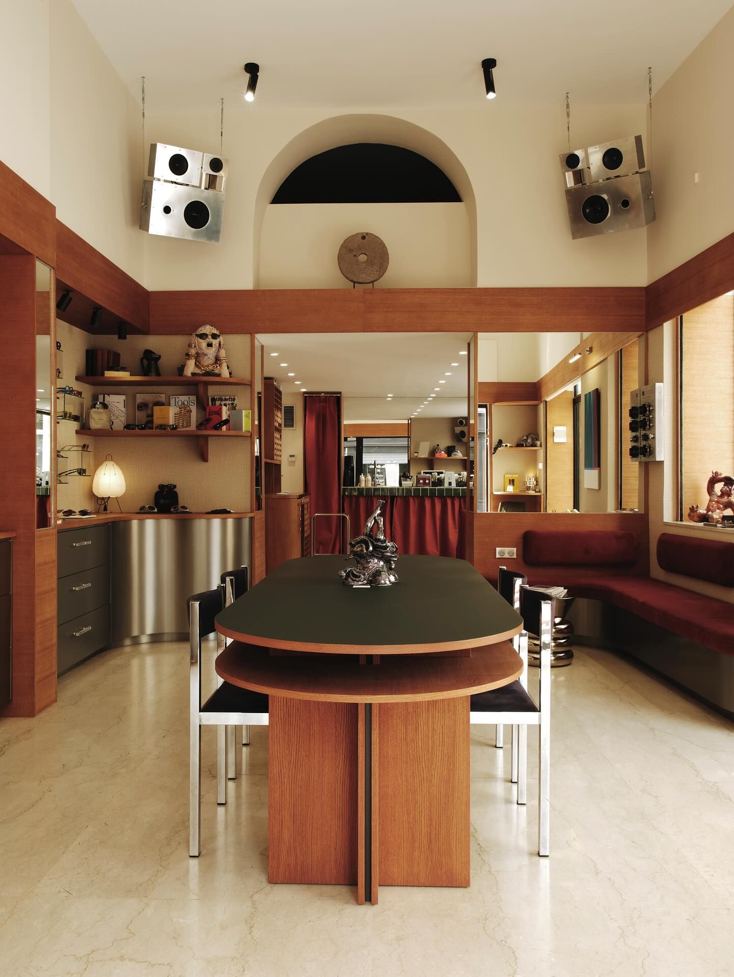 The salon at Focus Focus in Marseille, with a dark oval table, travertine floor, wood shelving and two chrome speakers under an arched window