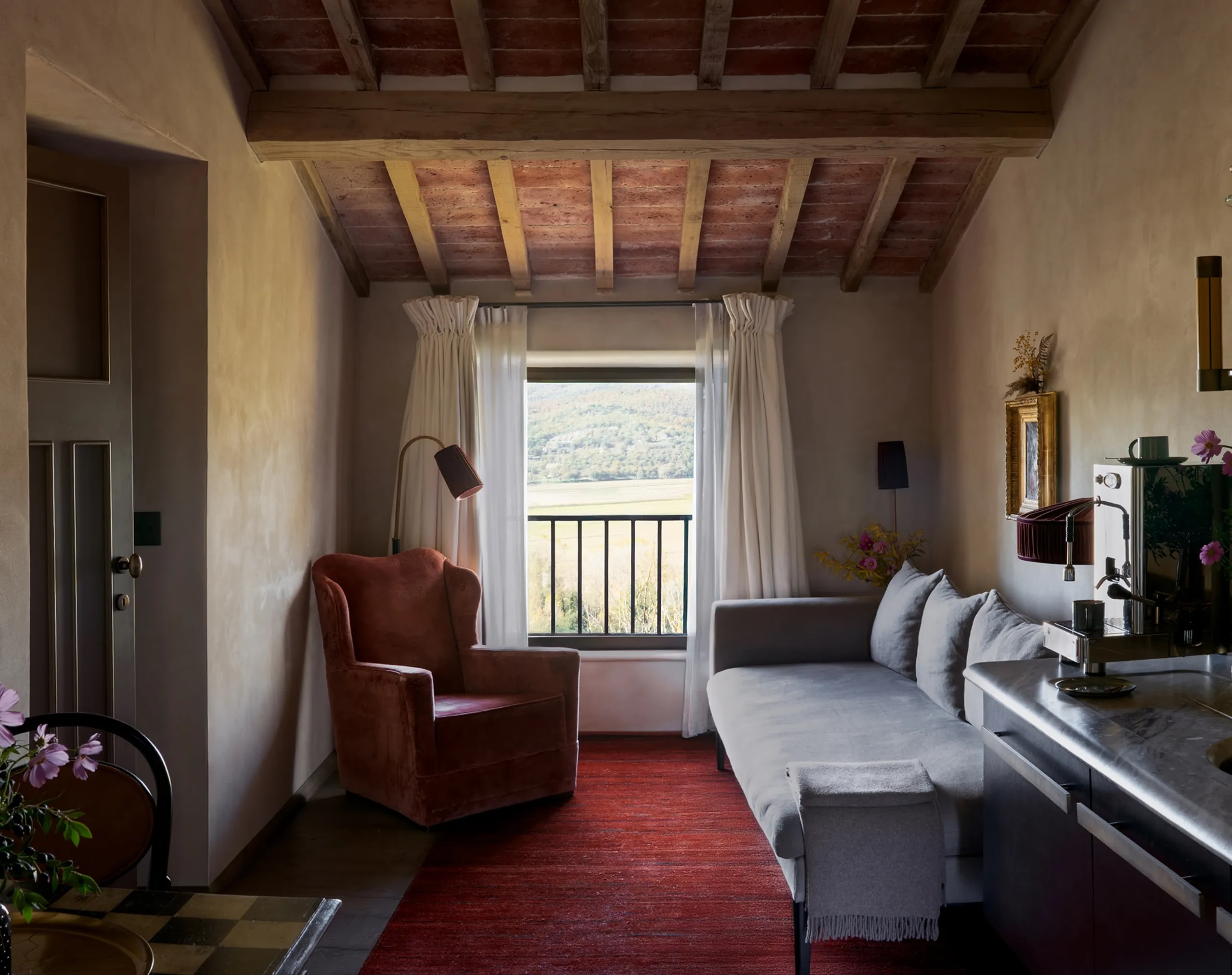 Castello di Reschio: a sitting room framed by a stone archway, with a red rug, an upholstered daybed, and garden light through tall windows