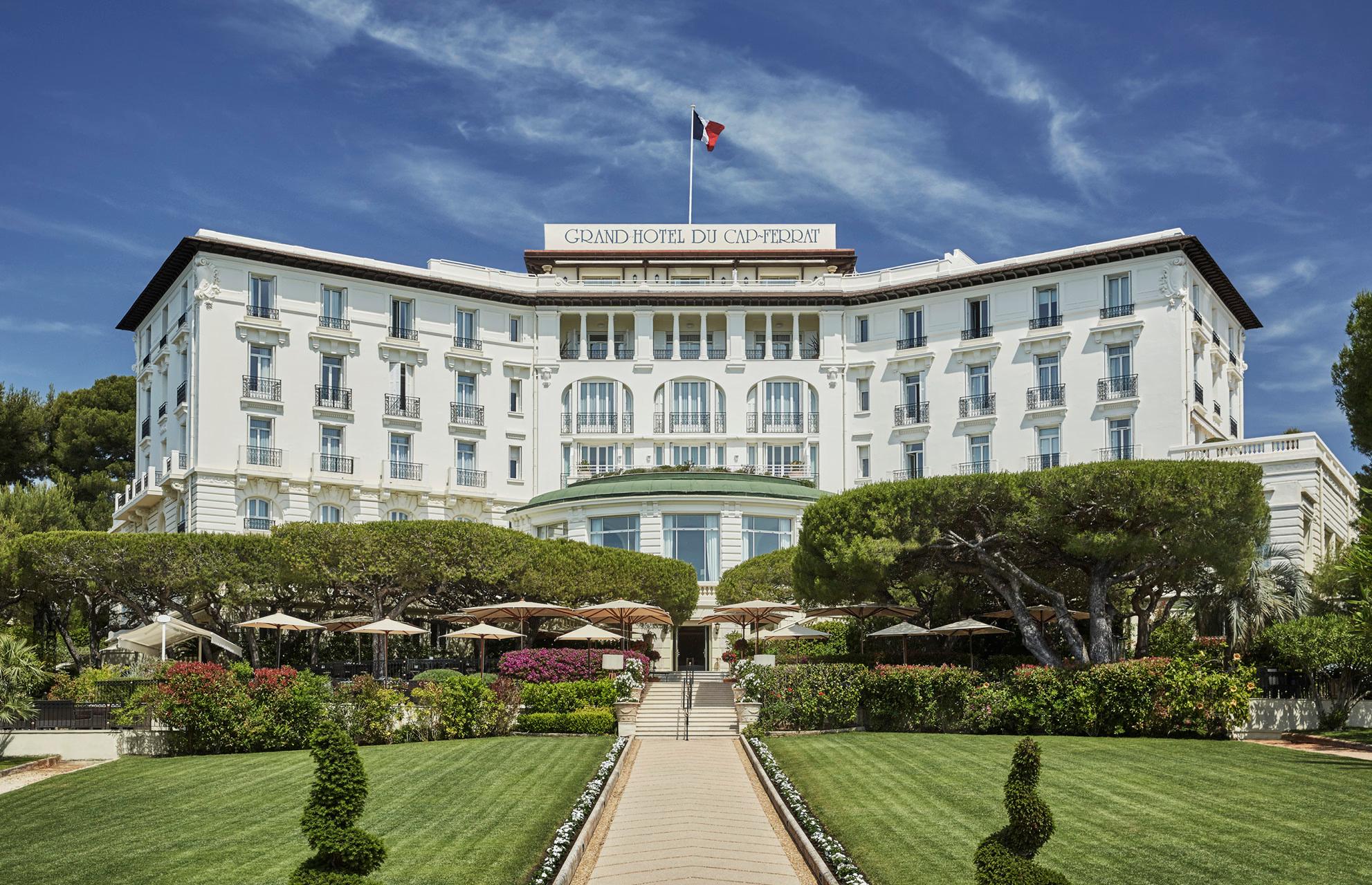 The cream-colored neoclassical facade rises above manicured gardens and lawn